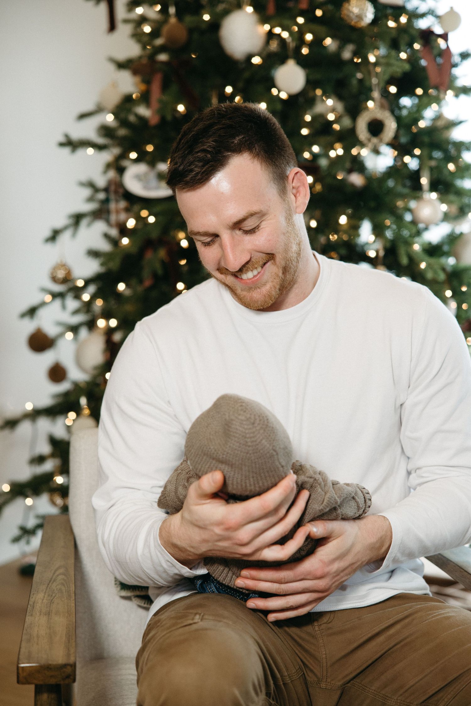 Close-up sequence of a person in white sweater holding and looking down with joy near a Christmas tree.