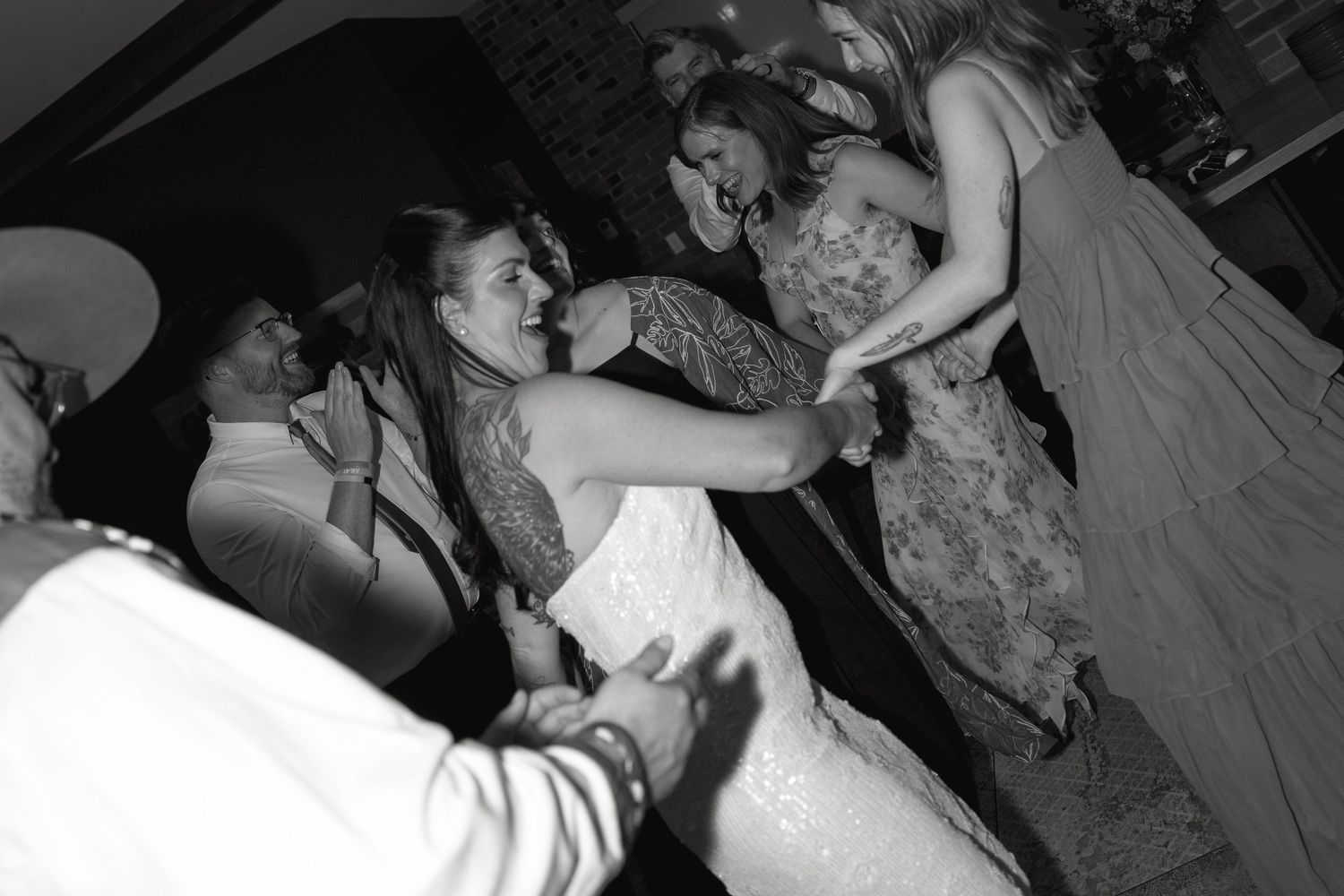 Black and white photo of guests dancing and laughing together on a crowded dance floor at a wedding reception party.