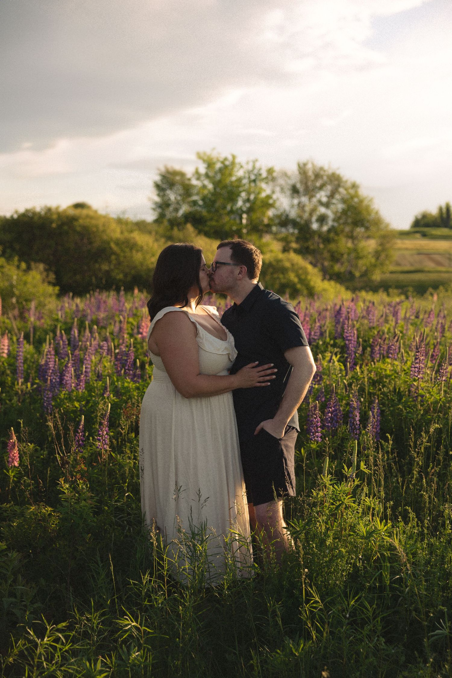 Couple sharing a kiss in a vibrant field of purple lupine flowers at golden hour.