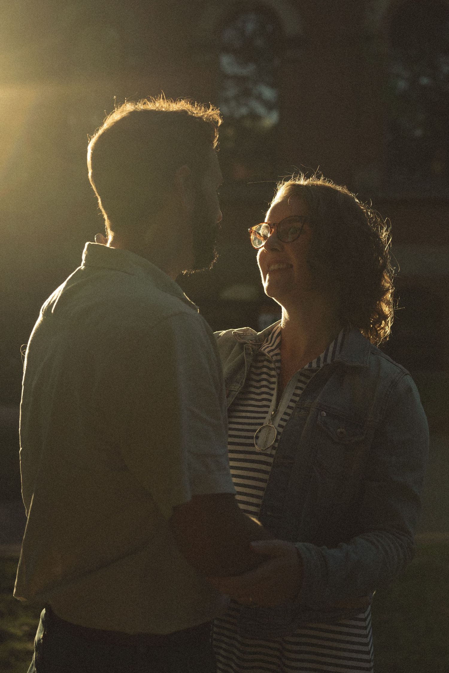A romantic couple embraces in golden sunset light against a dark background.
