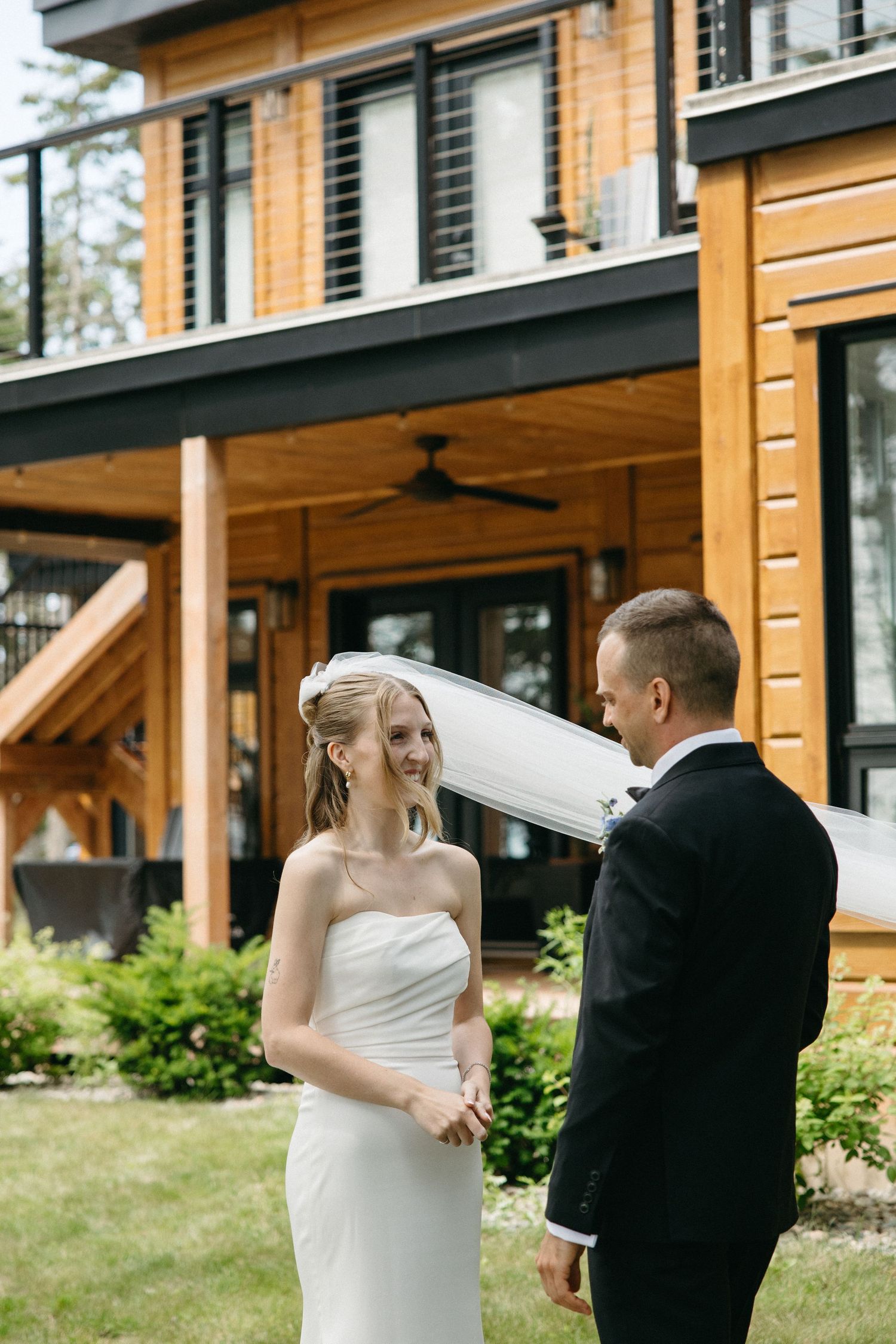 Bride and groom share a tender first look moment outside a modern wooden wedding venue on a sunny day.