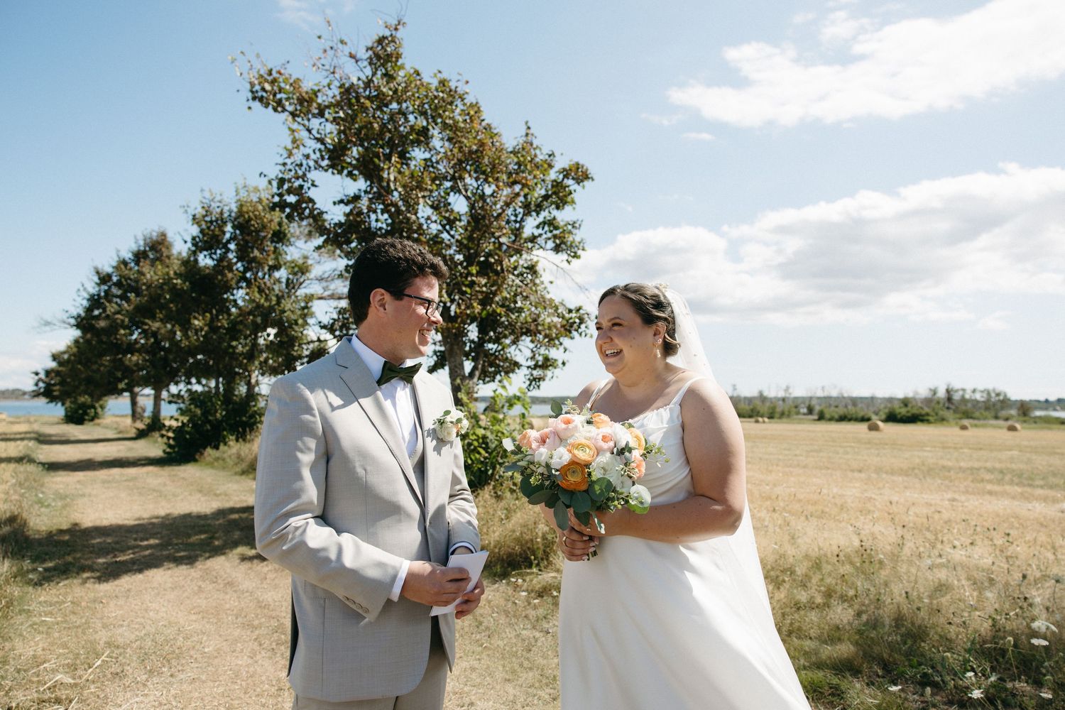 Bride and groom share a happy first look moment in sunny coastal field on their wedding day.