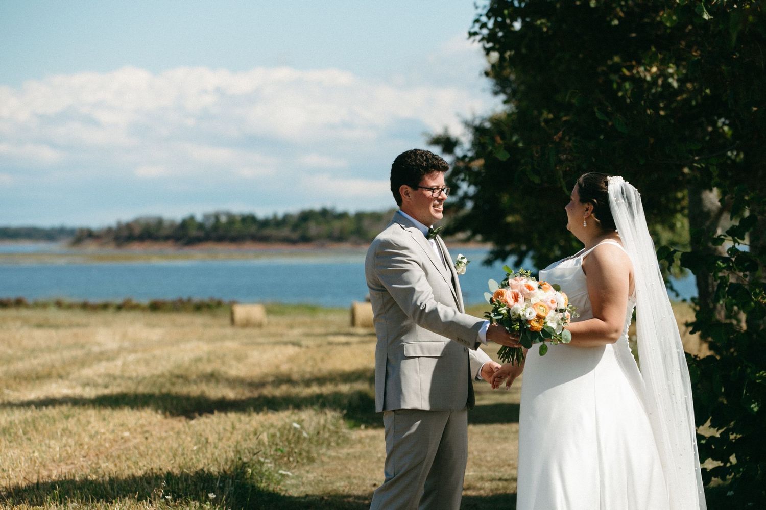 Bride and groom holding hands outdoors near a scenic waterfront on their wedding day.