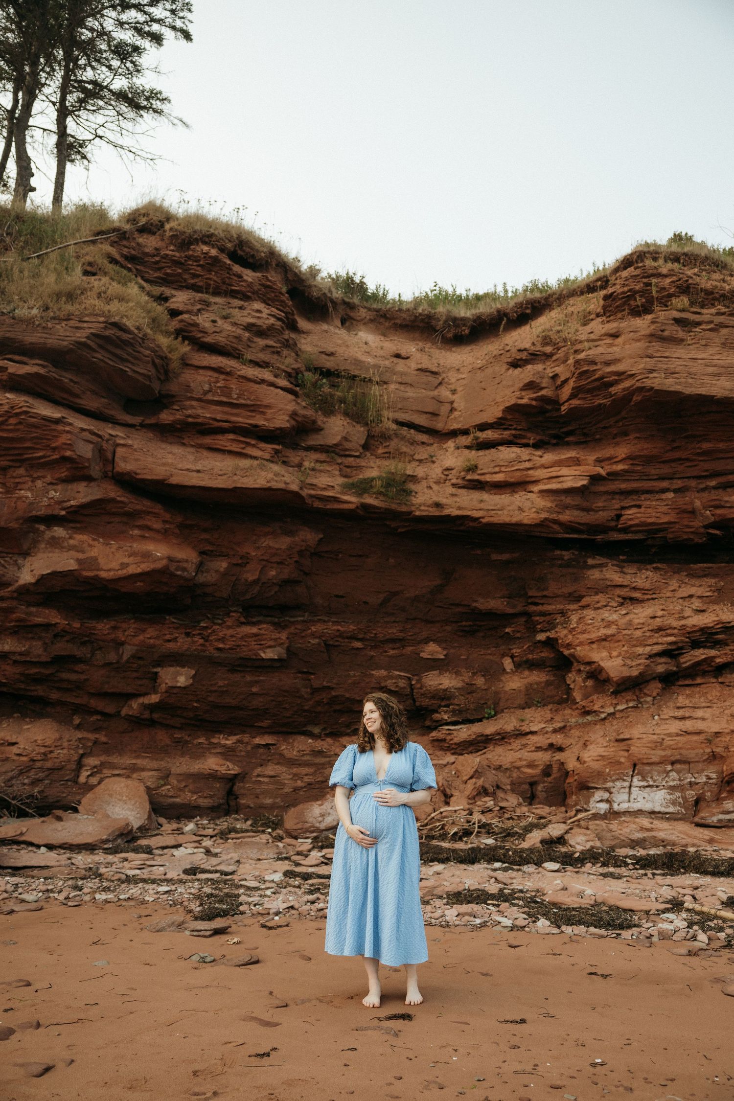 A scenic maternity photoshoot against red rock cliffs with someone in a flowing light blue dress posing elegantly.