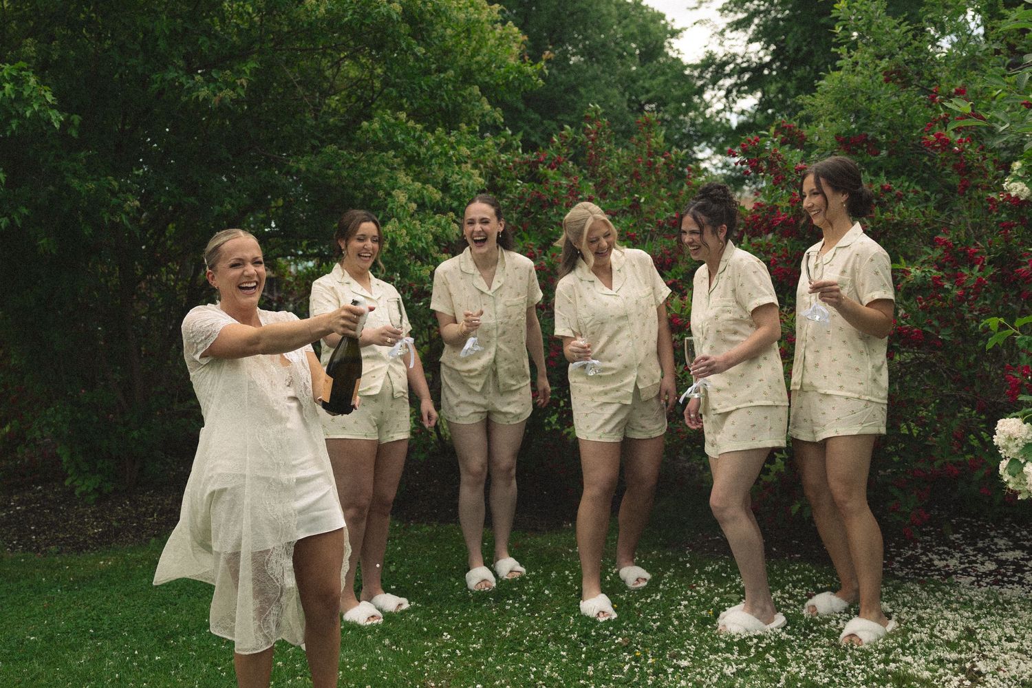 Wedding party in cream-colored attire posing together in a garden setting.