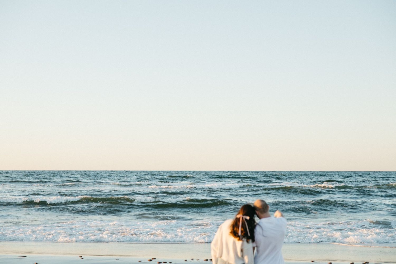 Couple embracing on a scenic beach with waves crashing in the background.