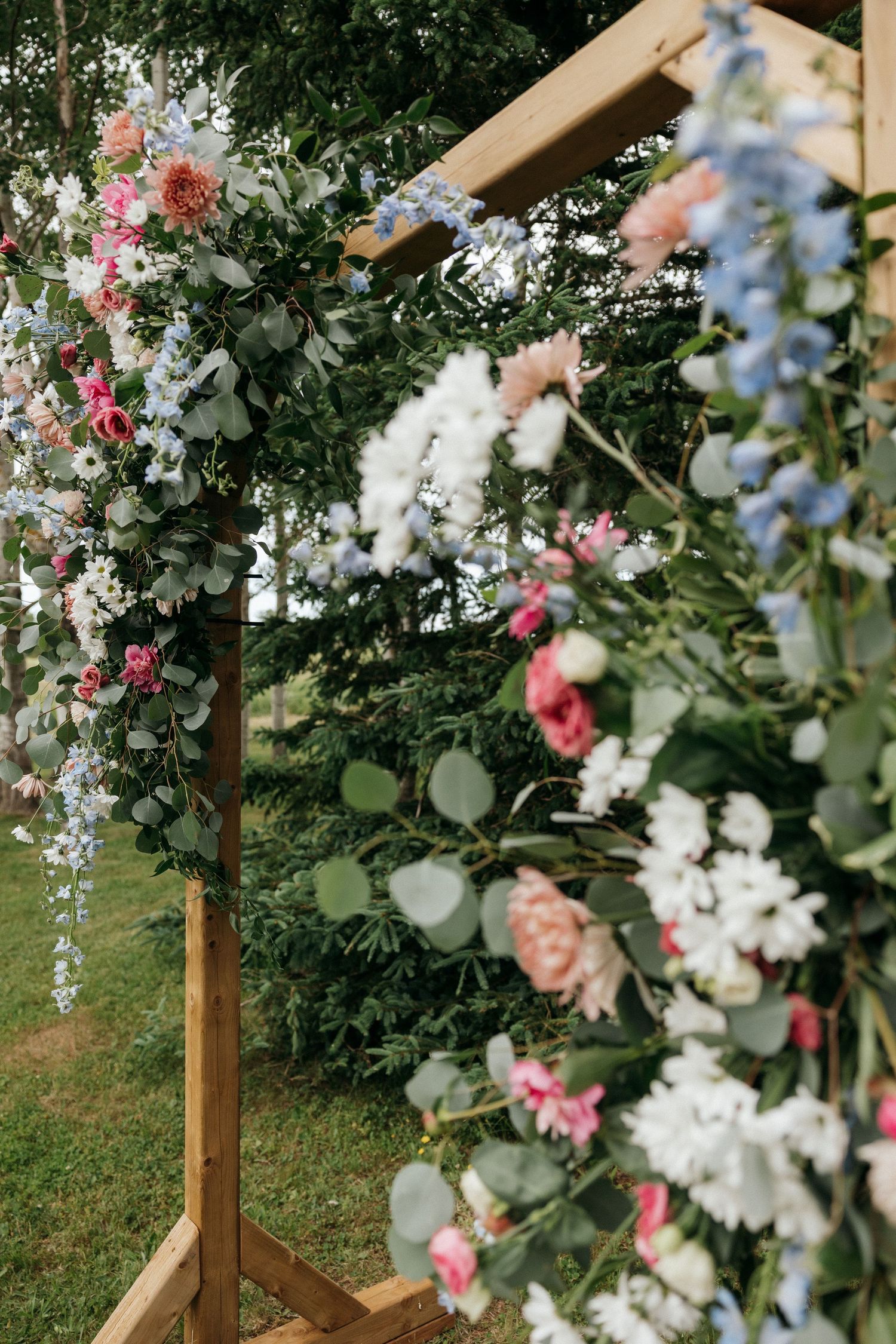 Floral arch with pink and white flowers decorates an outdoor wedding ceremony space.
