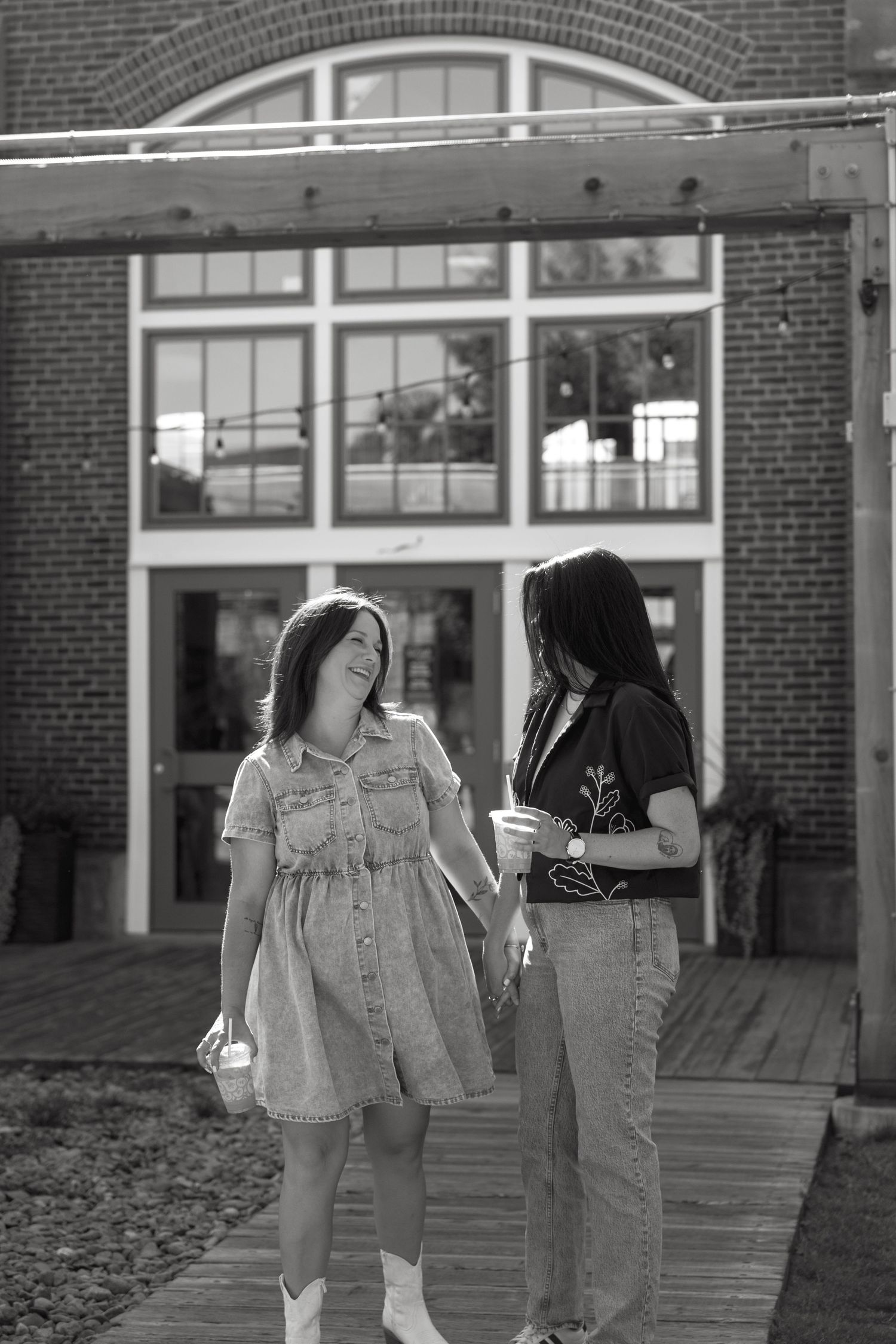 Two people walking together outside a brick building with large windows.