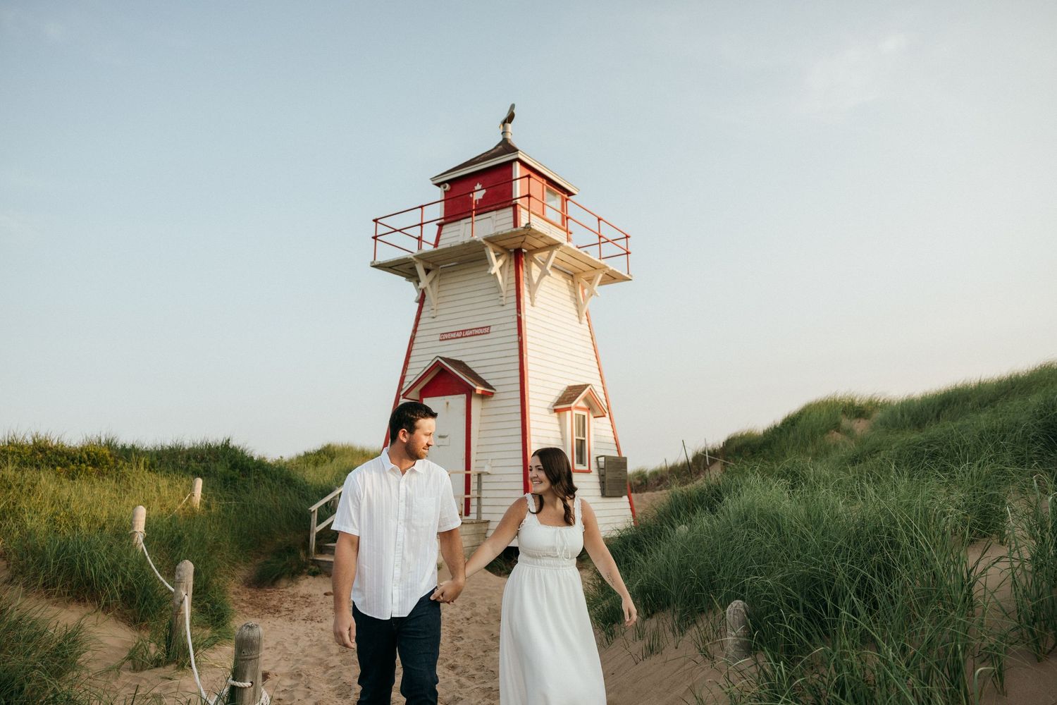 Red and white lighthouse standing tall on sandy dunes with grass in the foreground.