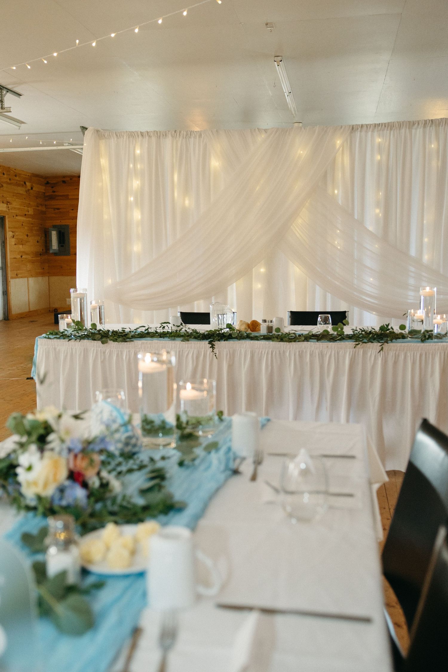 Elegant wedding reception tables decorated with blue accents, white linens, and twinkling lights overhead.