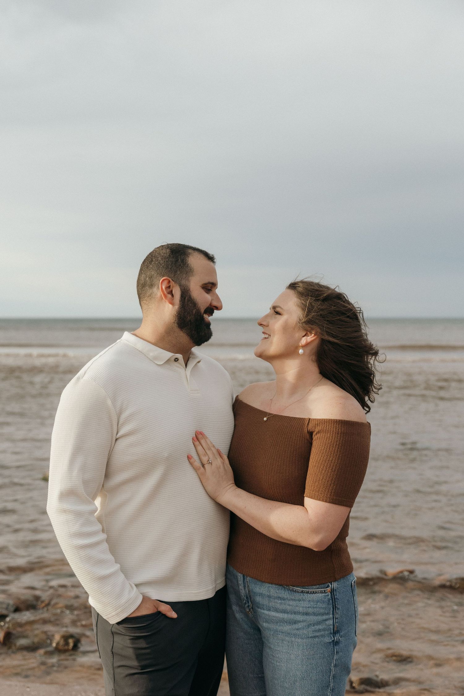 A couple shares intimate moments on a moody beach landscape with cloudy skies.