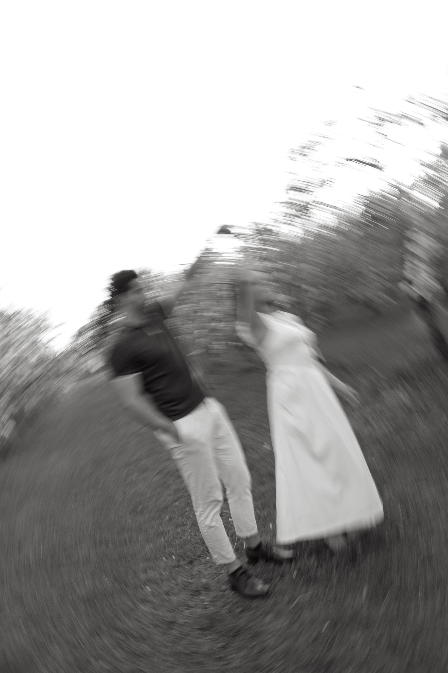 Black and white motion blur photo of couple walking hand in hand through a blooming orchard.