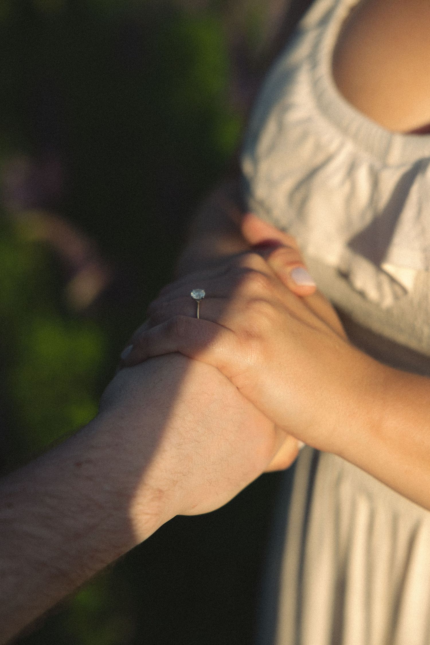 Close-up of couple holding hands showing elegant aquamarine engagement ring in warm sunlight.