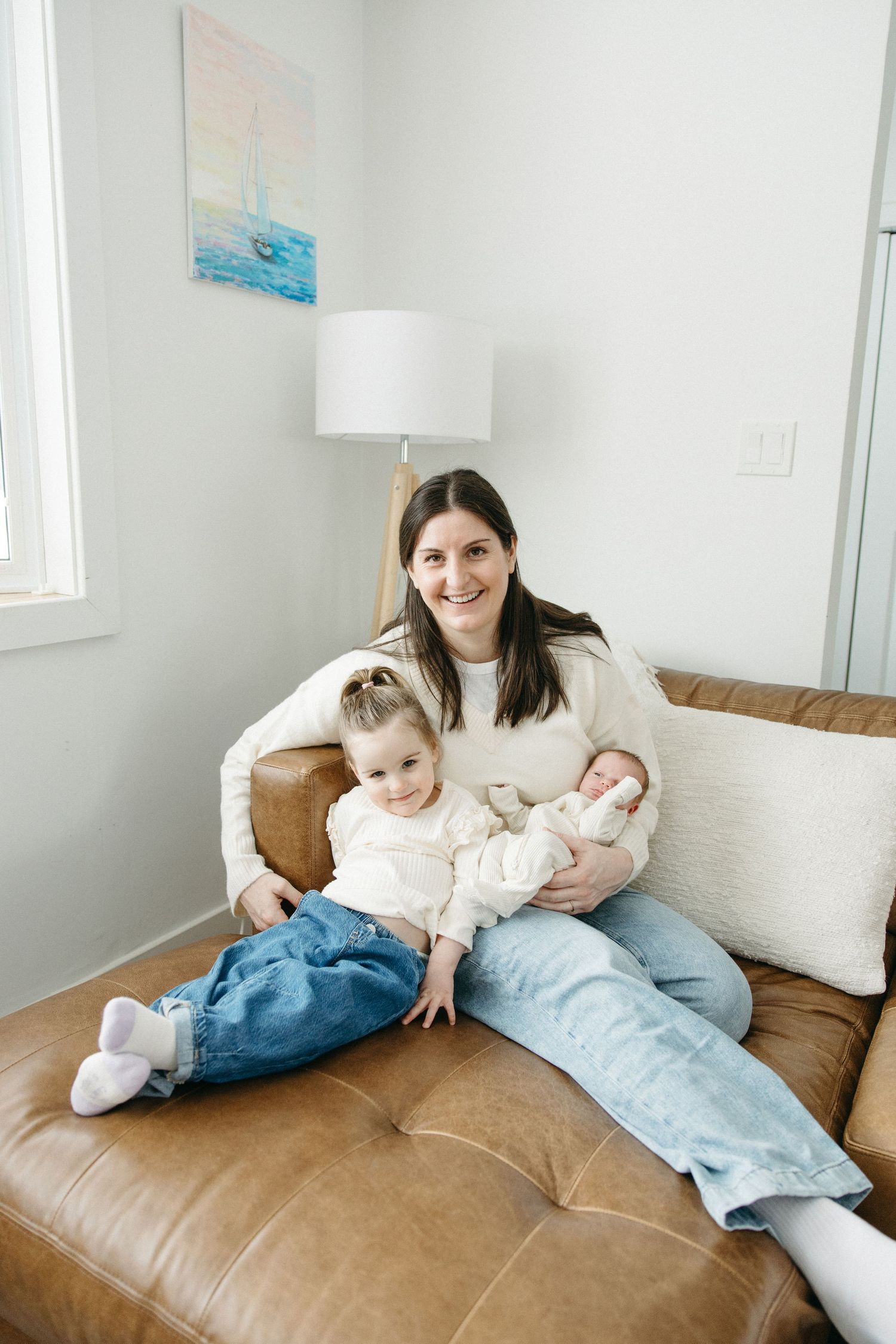 Family members lounging together on a brown couch in a bright, minimalist living room.