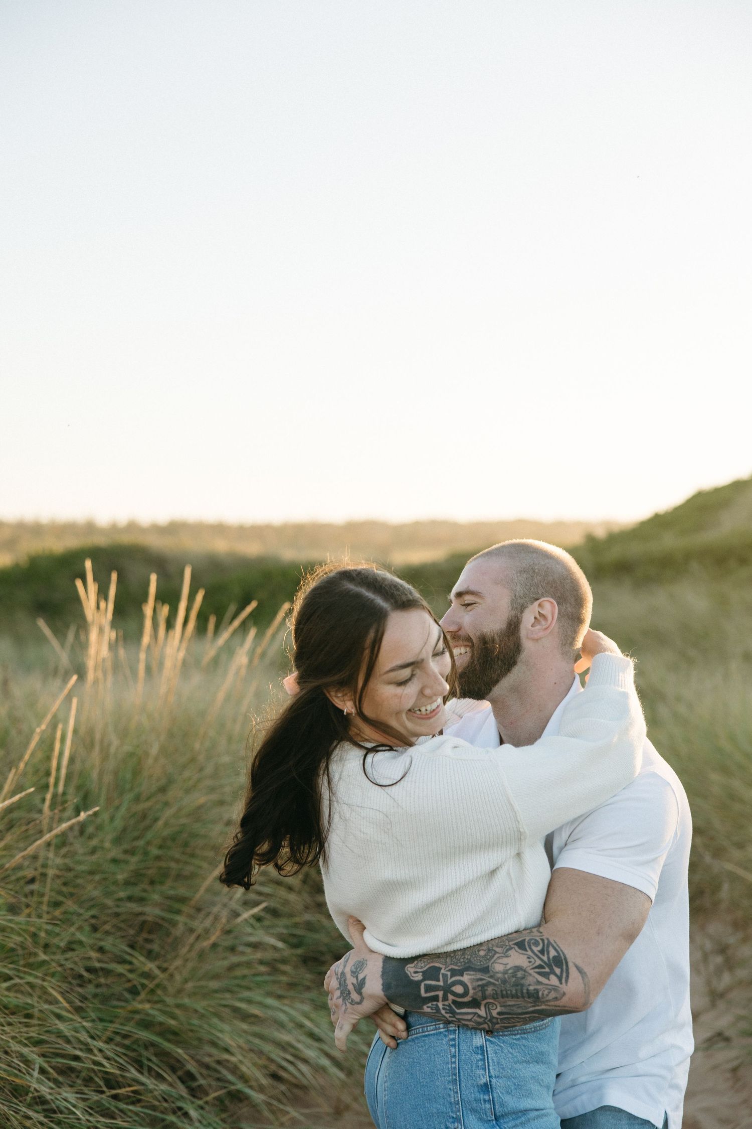 Joyful couple laughing together among beach grass at golden hour.