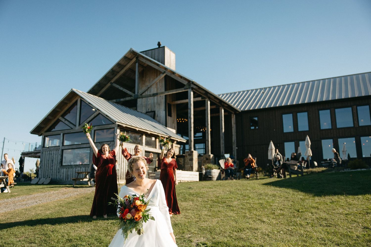 Guests celebrate at an outdoor wedding ceremony on a hilltop venue with modern architecture.
