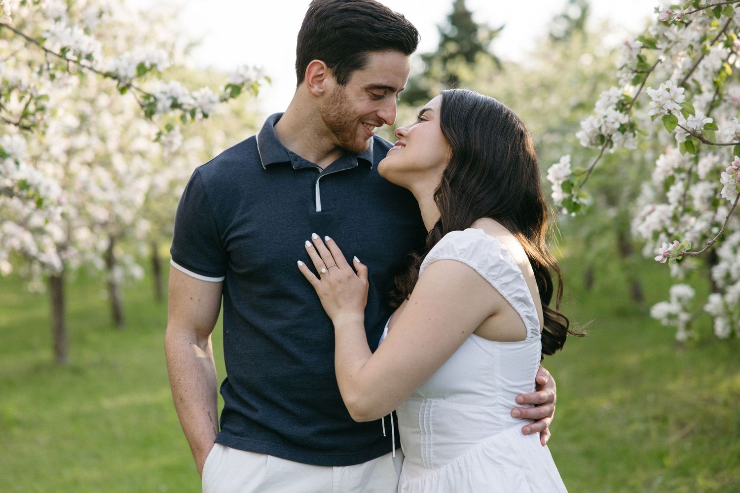 Loving couple embracing and smiling together among white flowering trees in spring garden.
