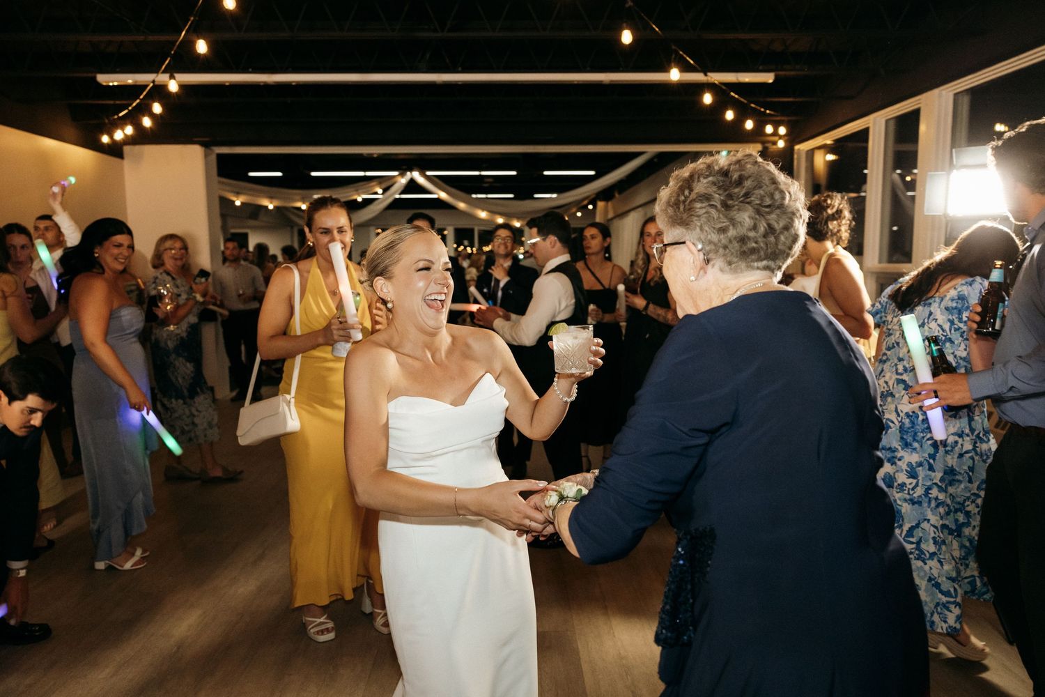Wedding guests dancing and celebrating on a dark dance floor with ambient lighting.