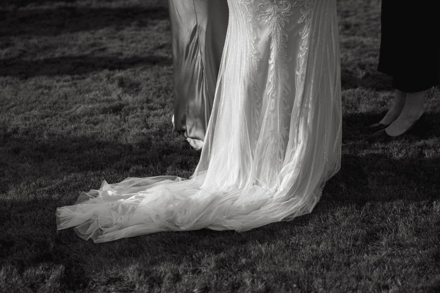Details of flowing white wedding dress fabric against grassy outdoor backdrop.