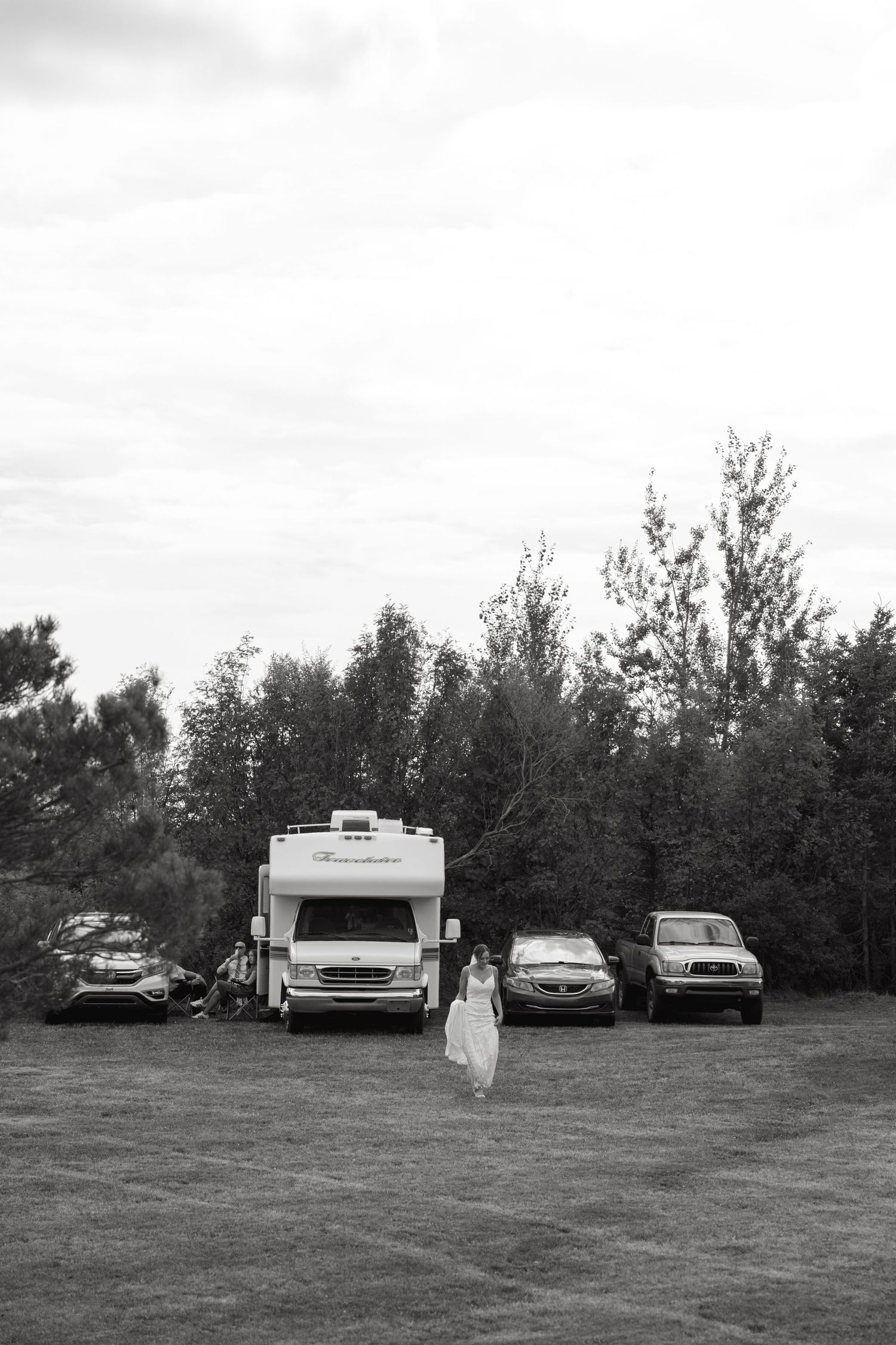 Black and white landscape view of RVs and cars parked in a grassy field.