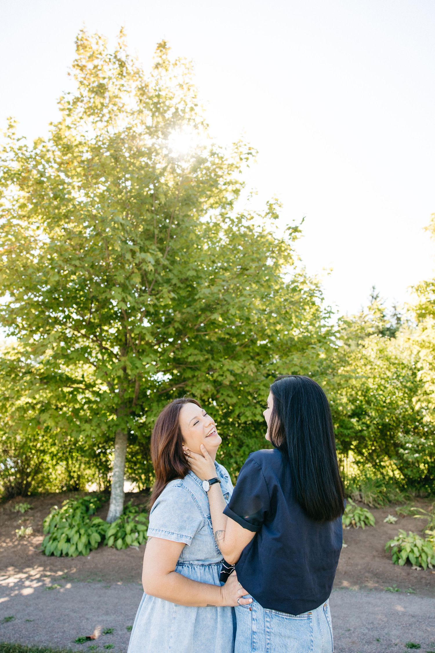 Couple embracing in a garden setting with sunlight filtering through trees.