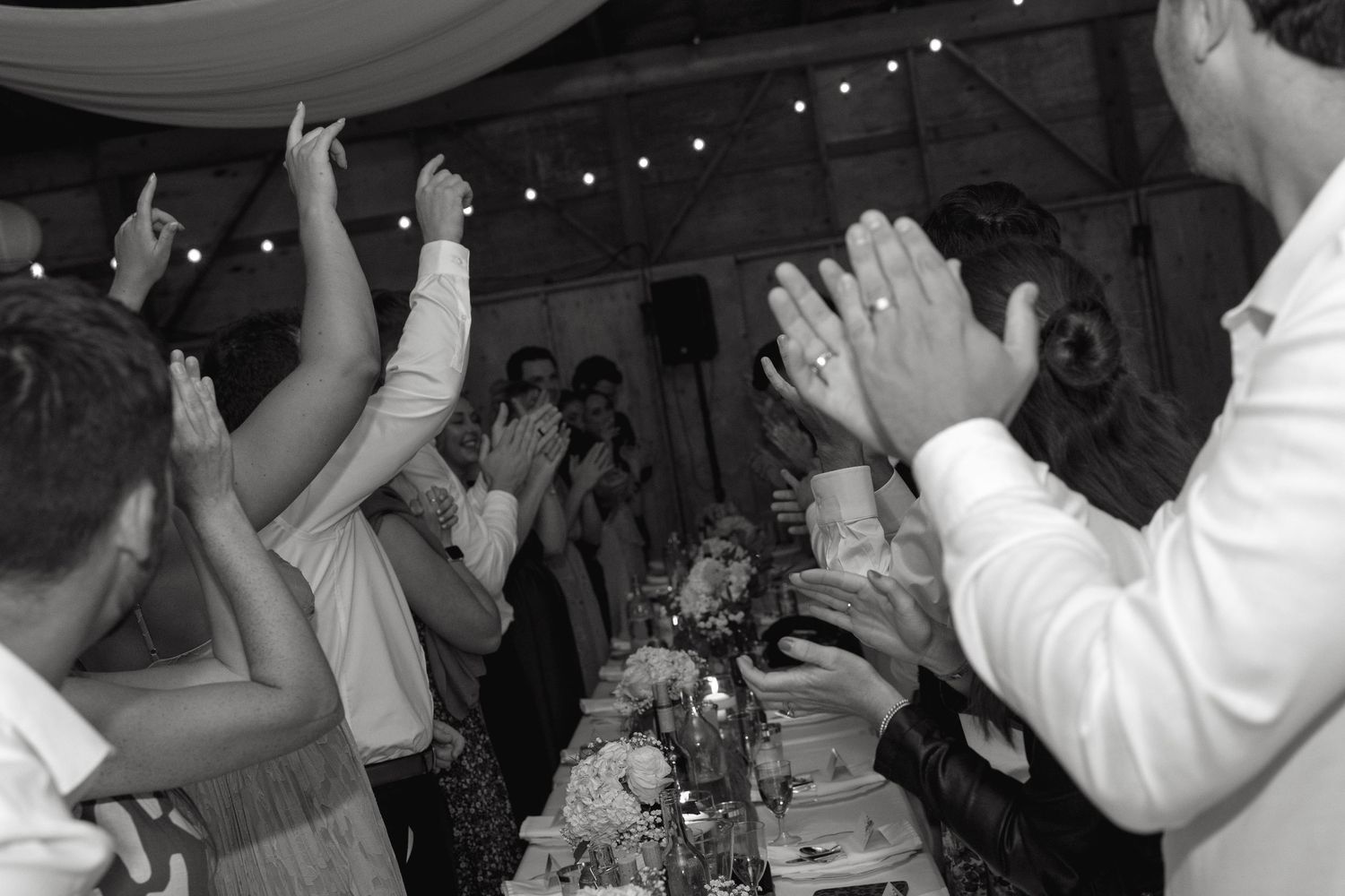 Wedding guests dance and celebrate on a dimly lit dance floor with string lights overhead.