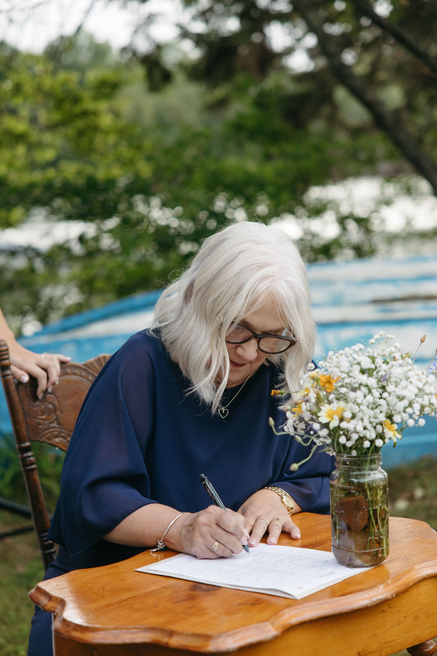Person in navy blue writing at wooden table with wildflowers in mason jar.