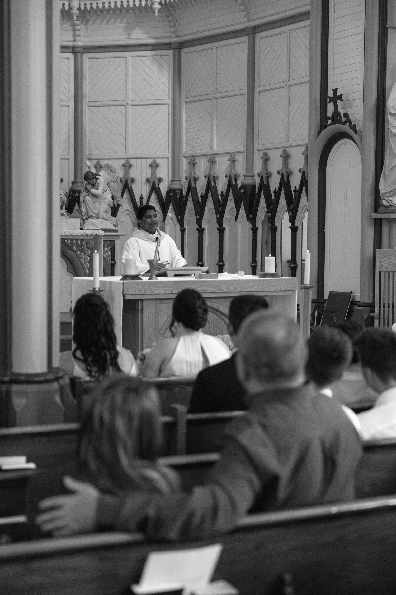 Black and white photo of guests seated in church pews during a wedding ceremony.