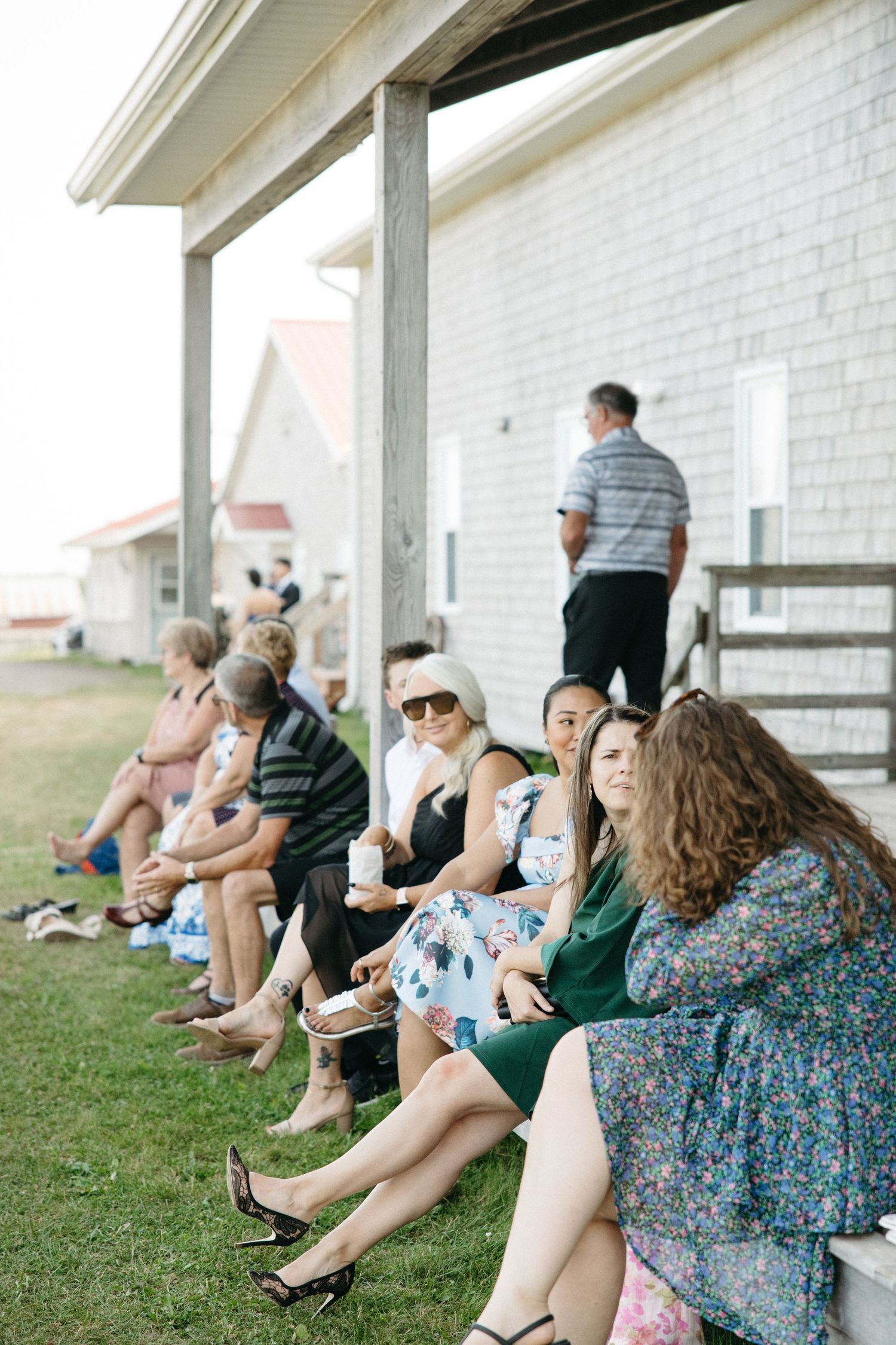 Group of guests relaxing on steps outside a white building during an outdoor event.