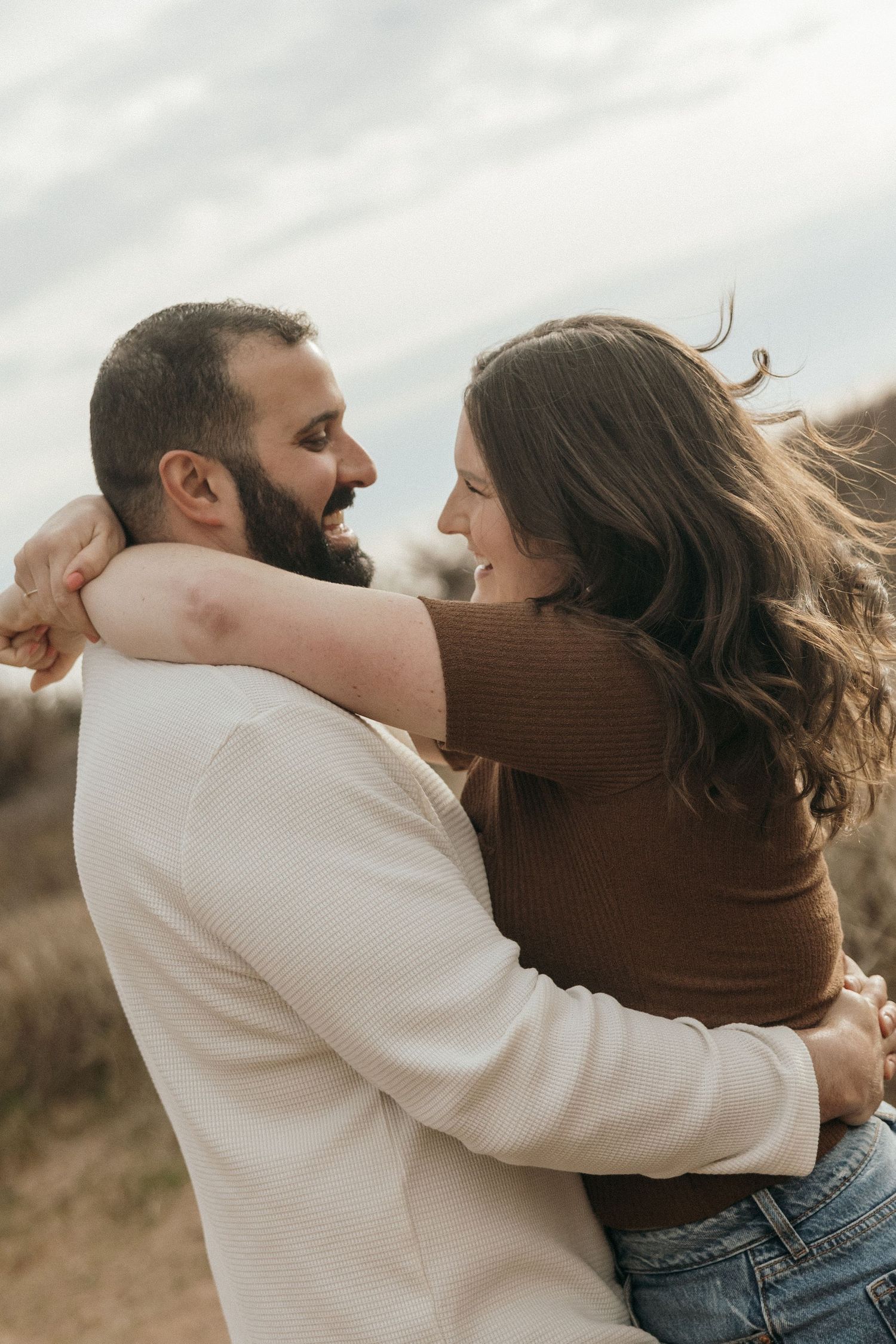 Couple in casual attire dancing and embracing on a cloudy day.