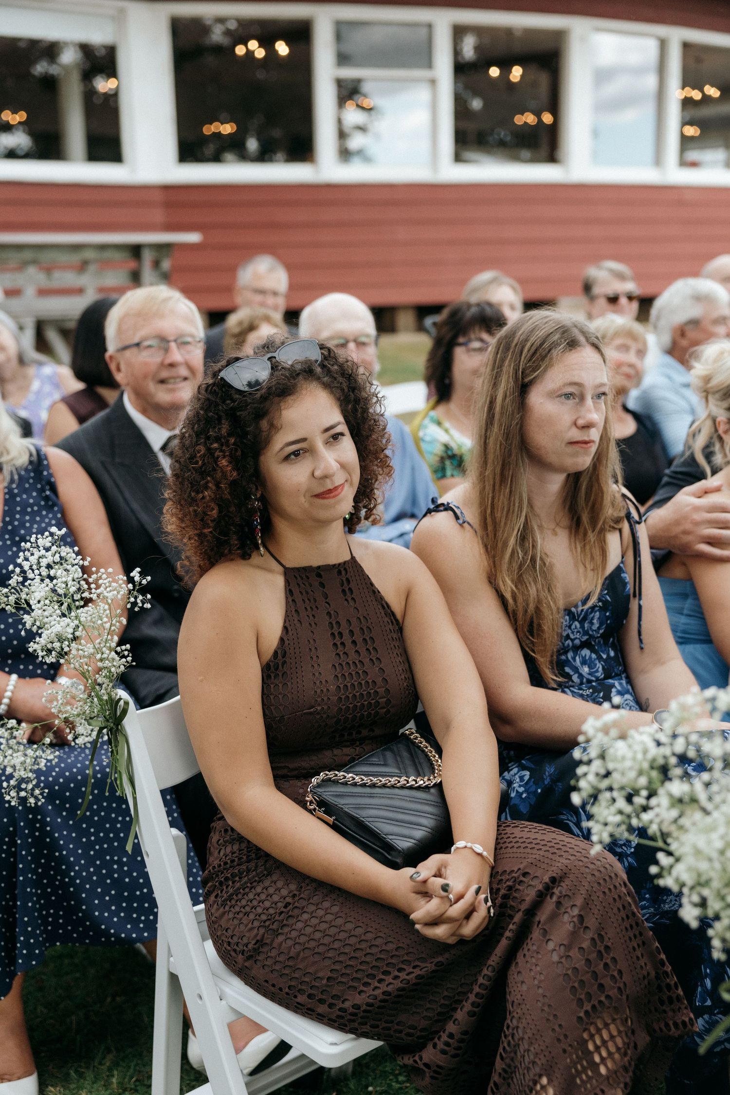 Wedding guests seated outdoors holding baby's breath bouquets during a ceremony.
