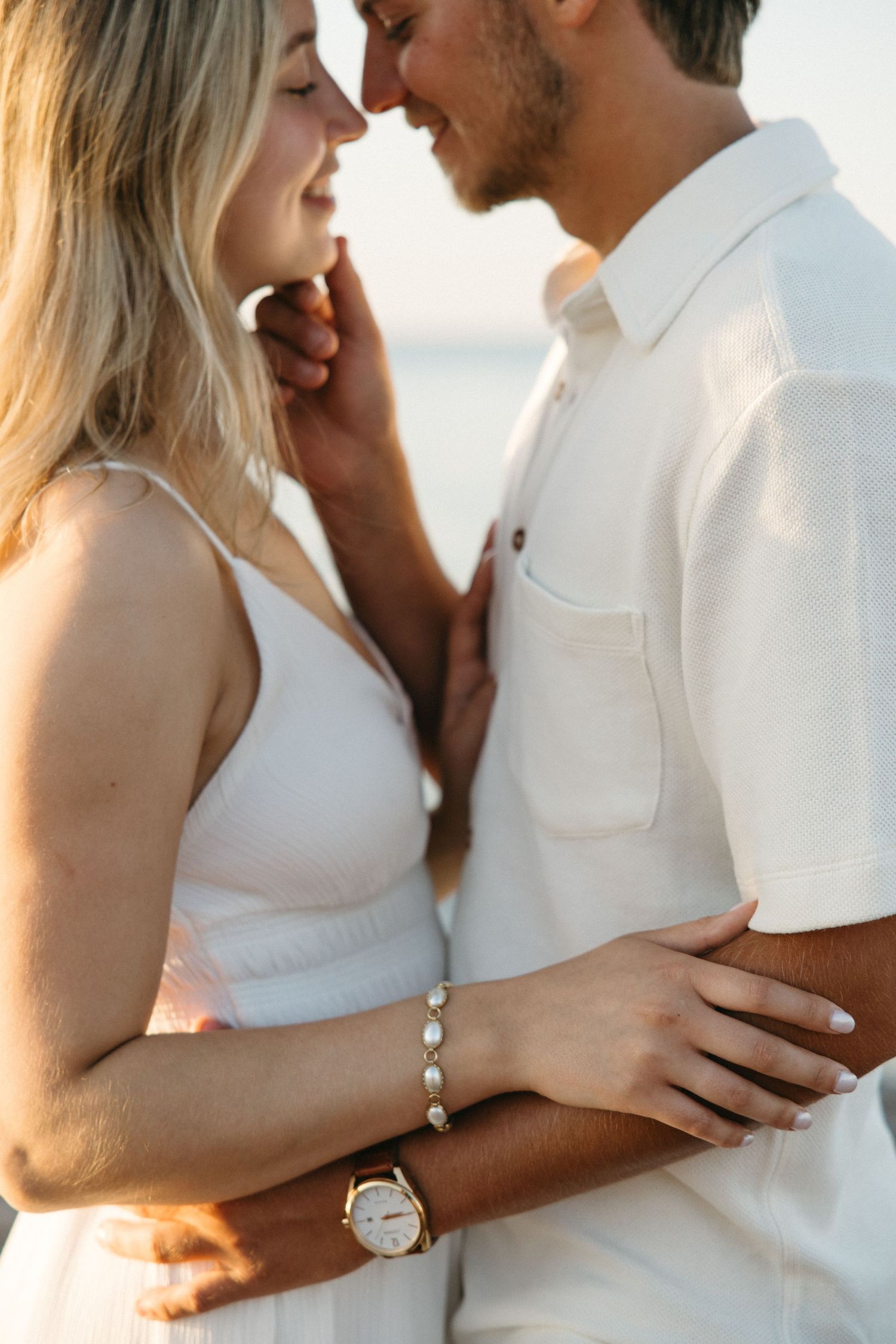 Romantic couple in white outfits sharing a close moment at sunset beach.