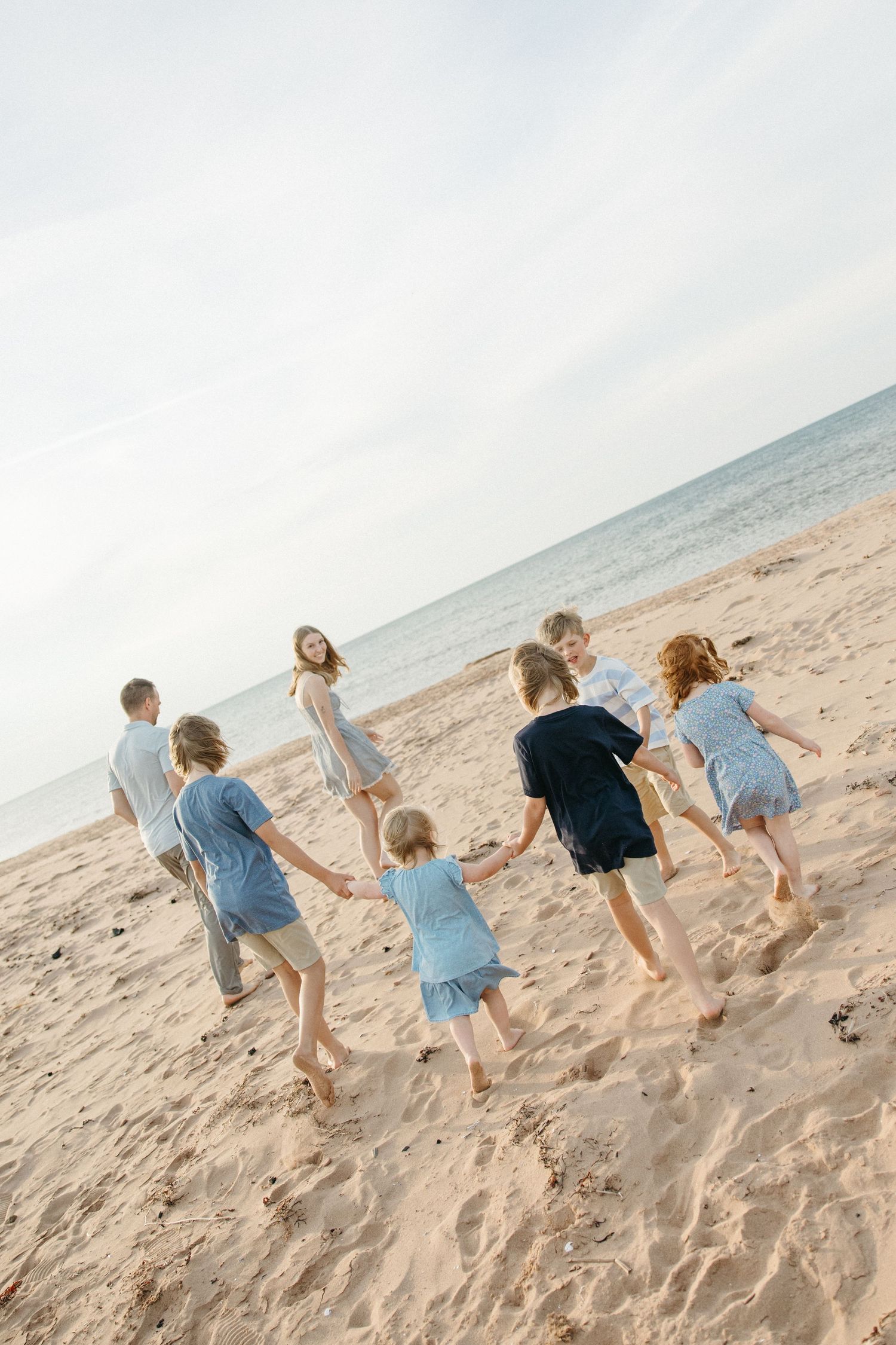 Children holding hands and playing in a circle on a sandy beach near the ocean on a cloudy day.