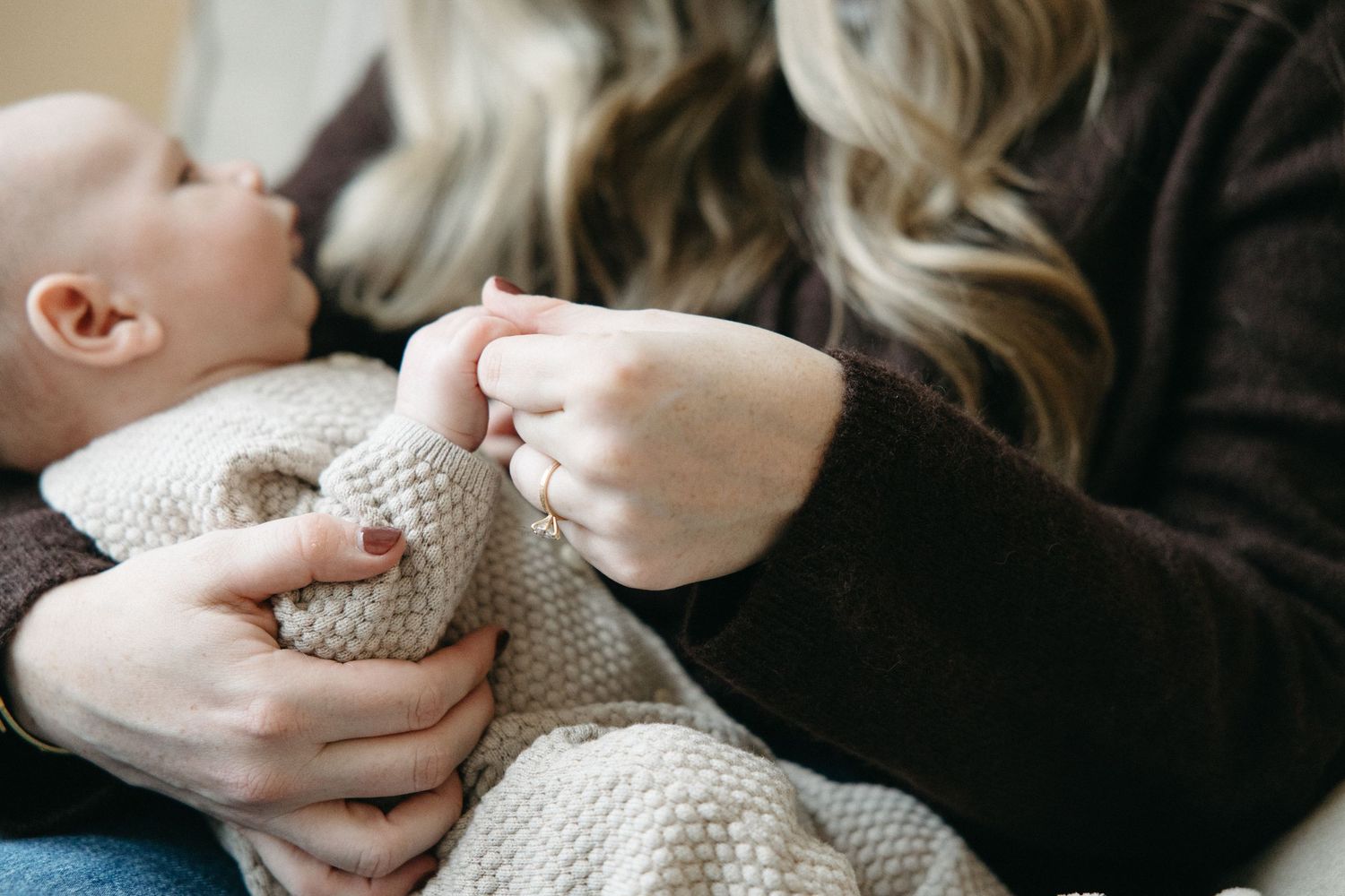 Gentle hands holding a newborn wrapped in knit blanket.