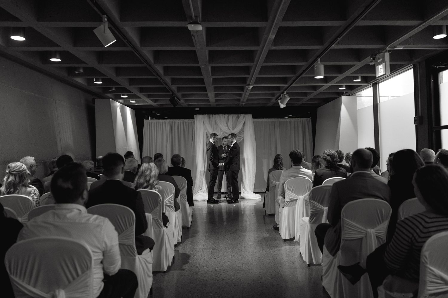 Interior view of wedding ceremony venue with rows of white chairs and guests seated.