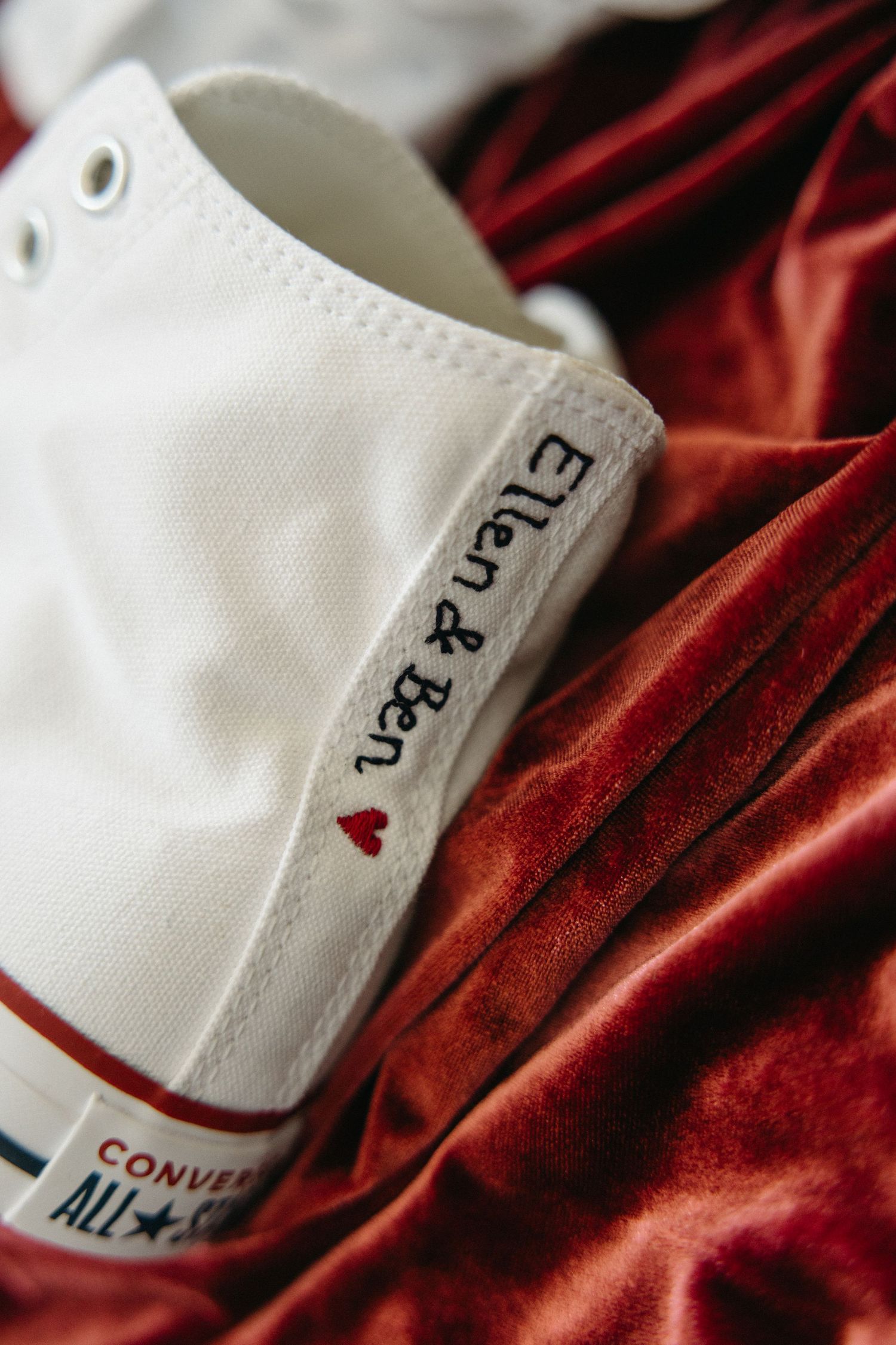White Converse sneaker with personalized text detail against red velvet fabric.