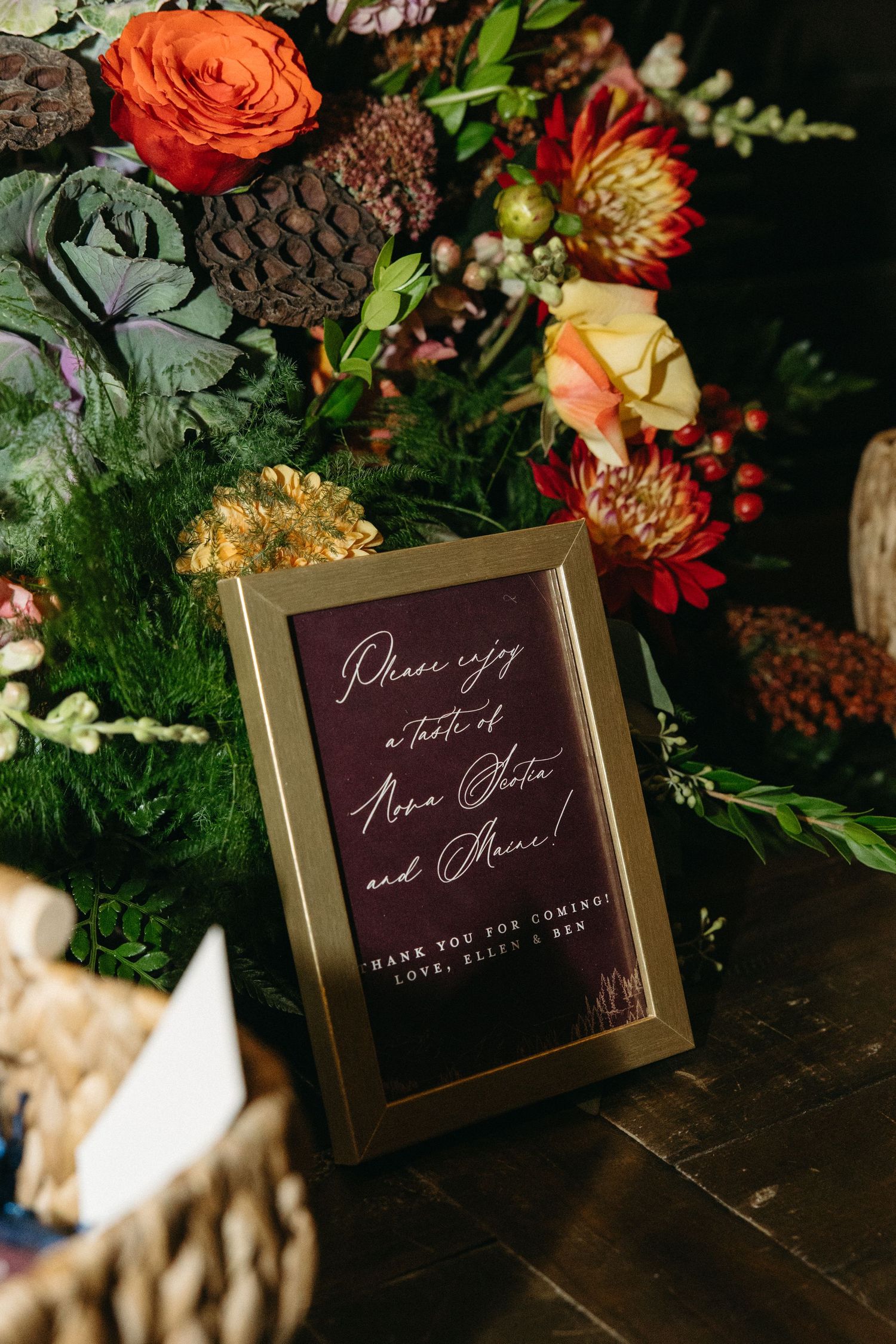 Wedding signage with burgundy and gold frames surrounded by orange and red floral arrangements.