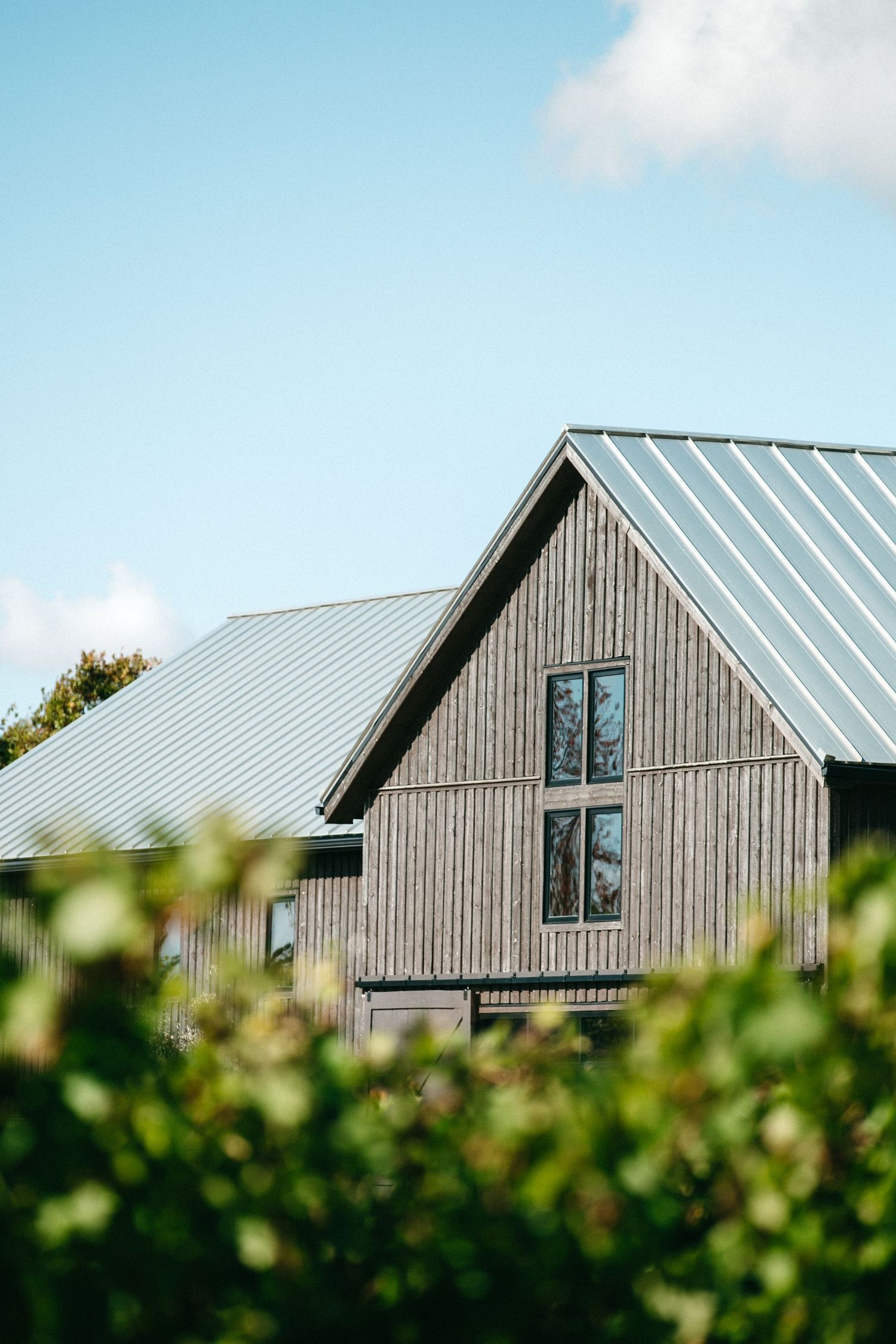 Modern barn-style building with vertical wood siding and metal roof against blue sky.