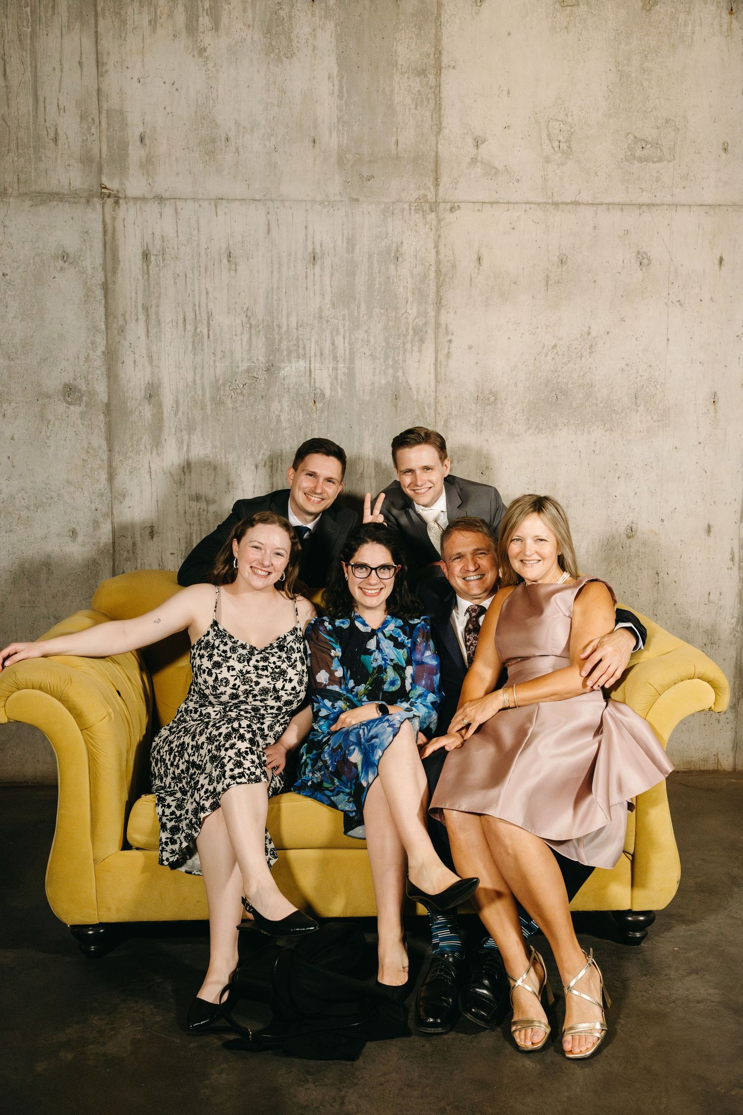 Wedding party members relax together on a bright yellow couch in an industrial space.