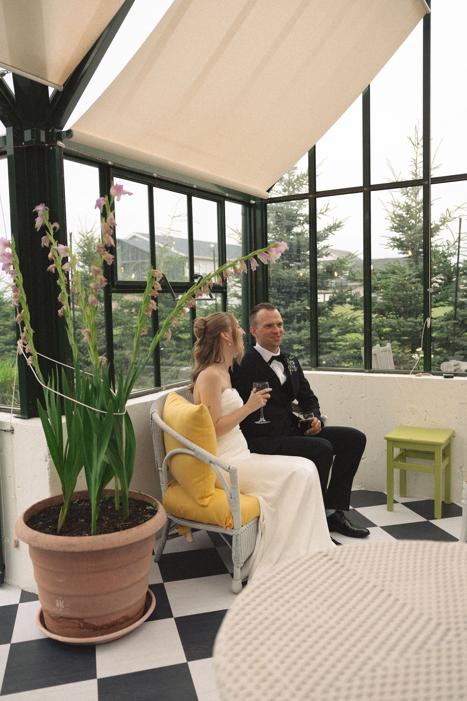 Bride and groom sitting together in a sunroom conservatory toasting with champagne glasses.