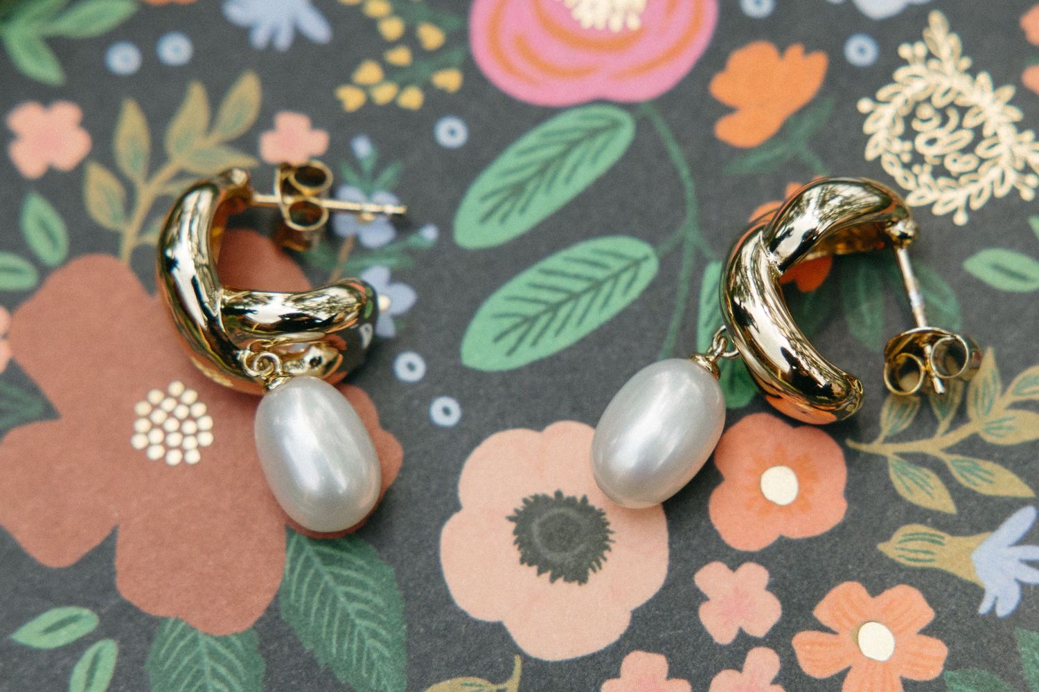 Elegant gold hoop earrings with pearl drops displayed on floral patterned background.