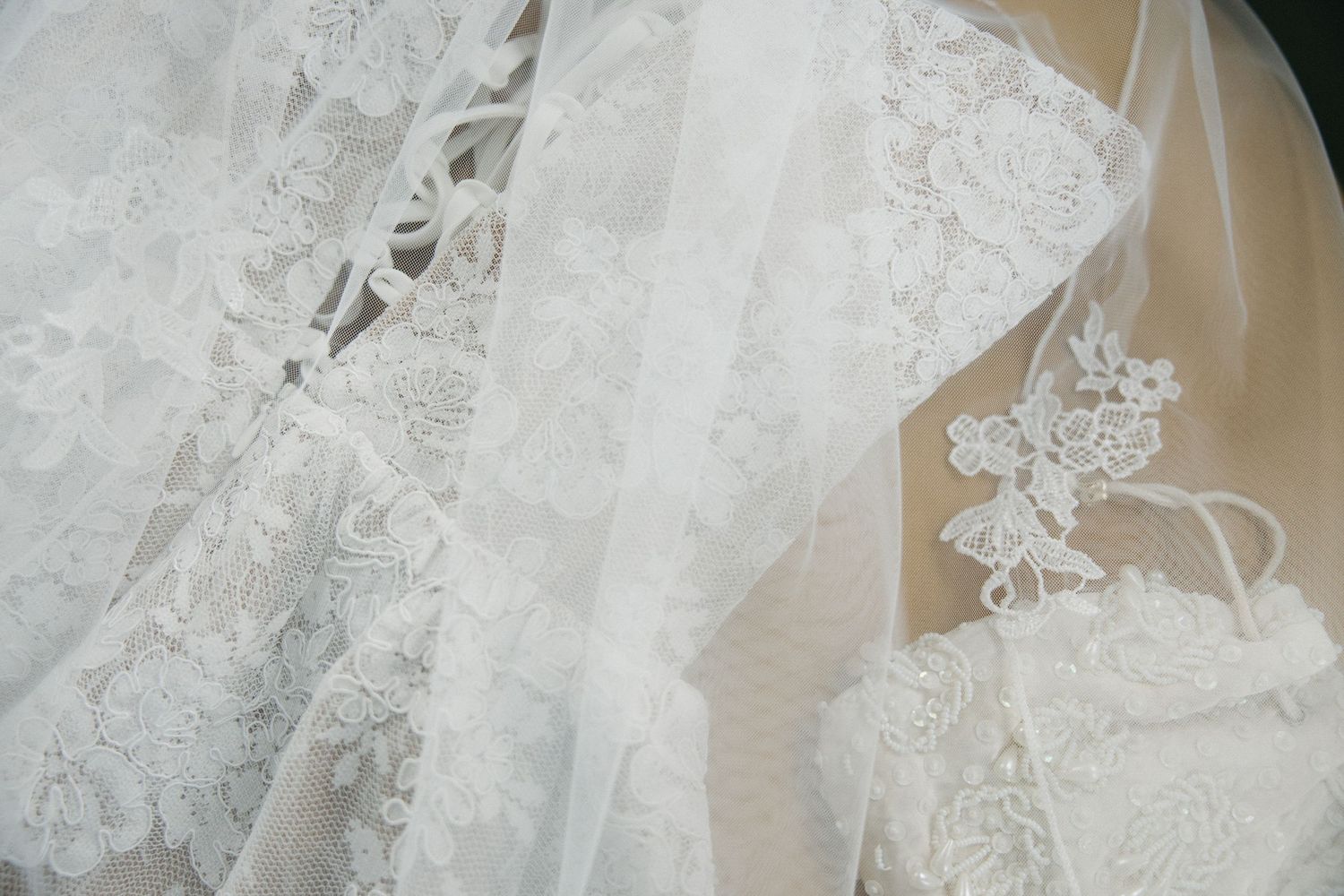 Close-up of elegant white lace wedding dress fabric with intricate floral embroidery and delicate tulle overlay.