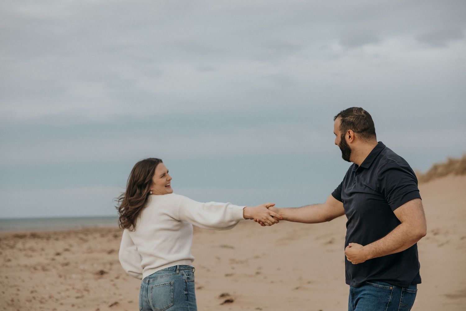 Couple playing and holding hands while walking on a sandy beach.