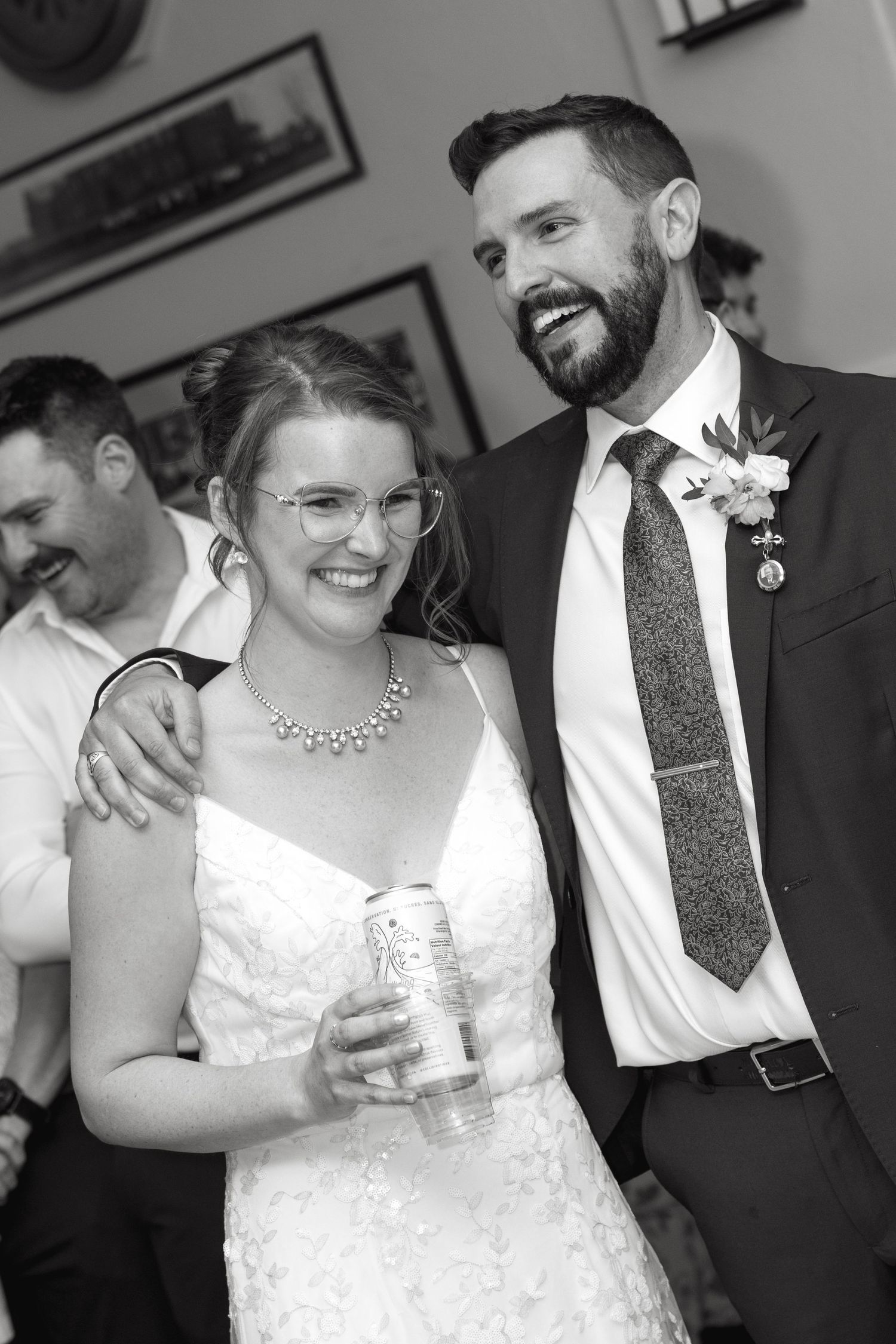 Black and white photo of a smiling bride and groom at their wedding reception, bride holding a drink can.