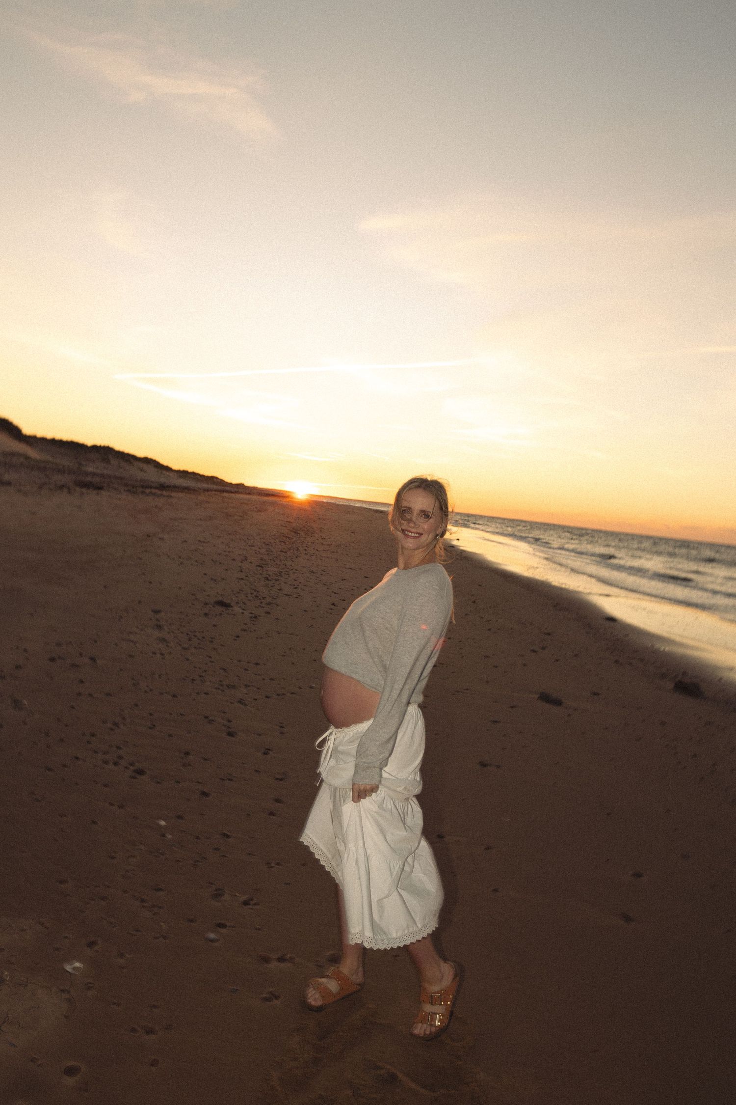 A person in white clothing twirls on a beach at sunset.