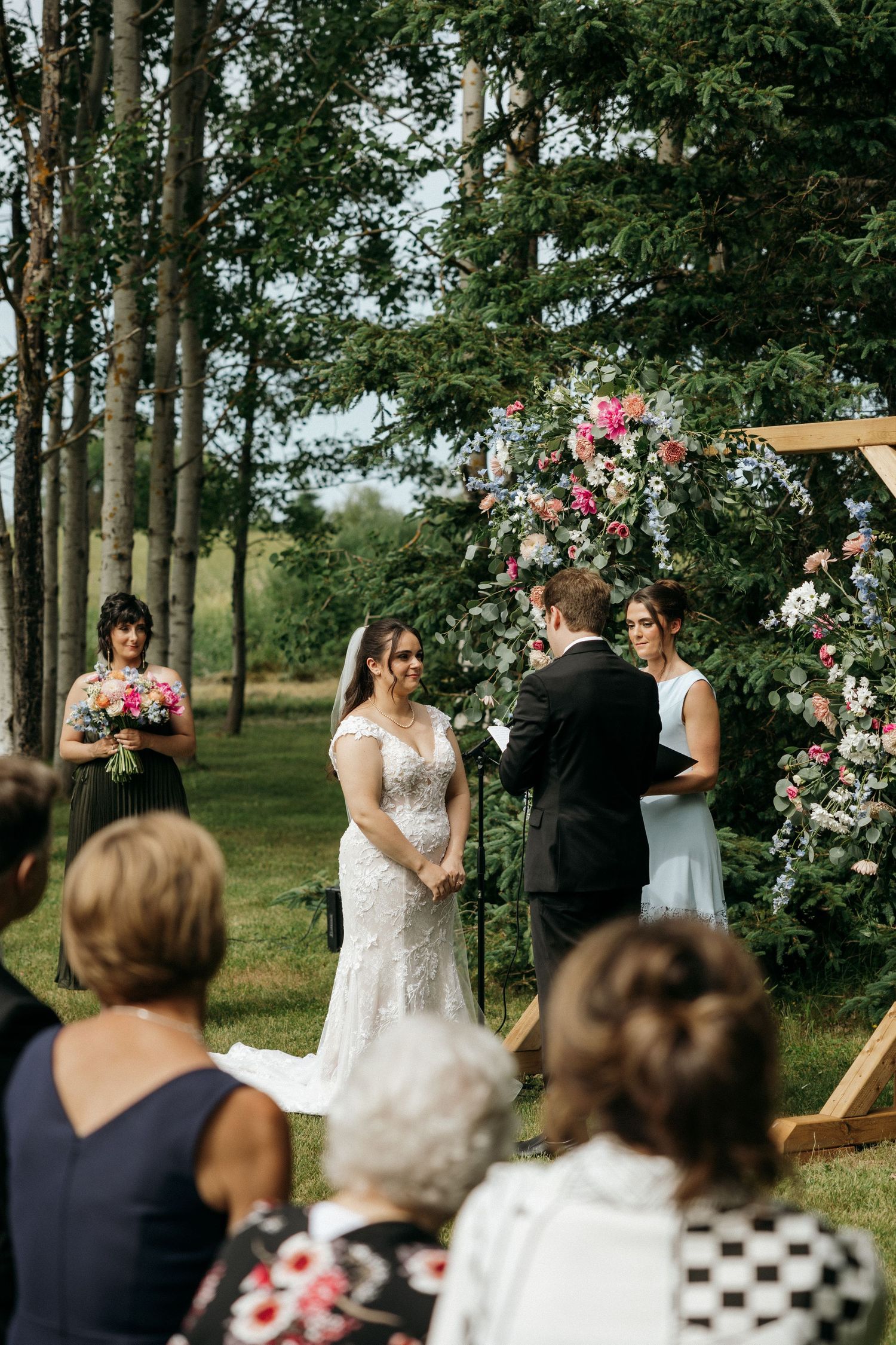 Wedding ceremony under wooden arch decorated with pink roses in natural forest setting.