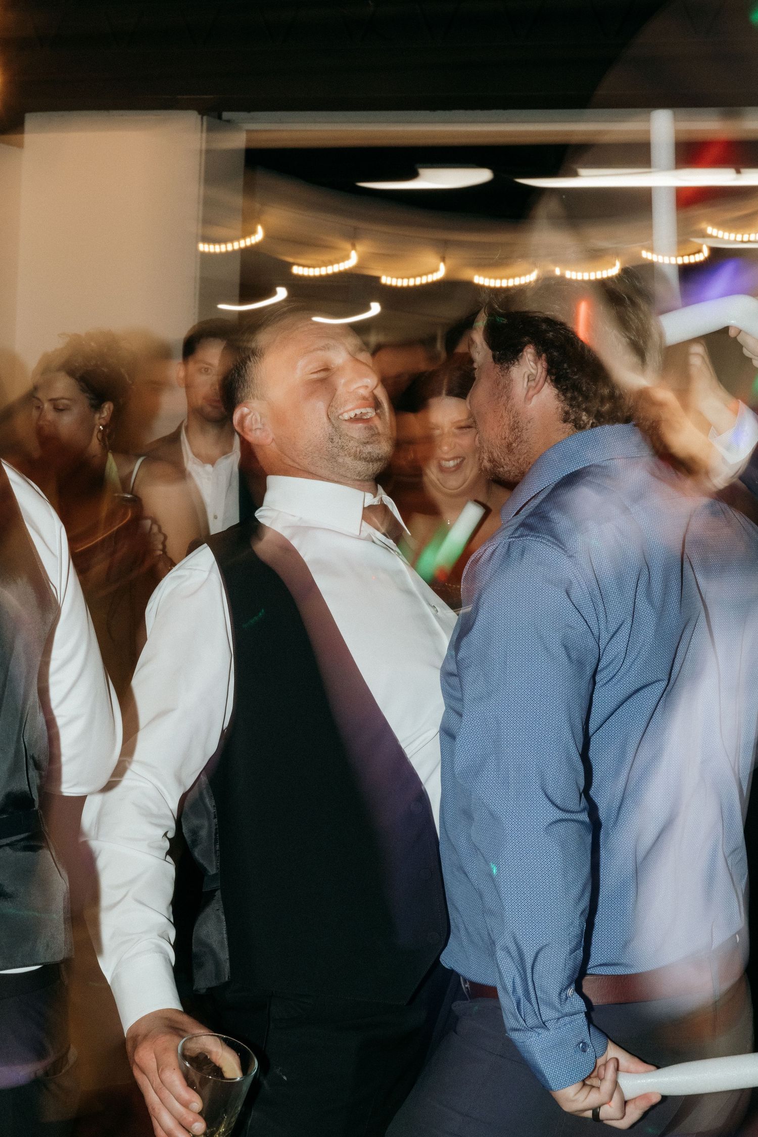 Blurred motion captures wedding guests dancing and celebrating at an indoor reception.