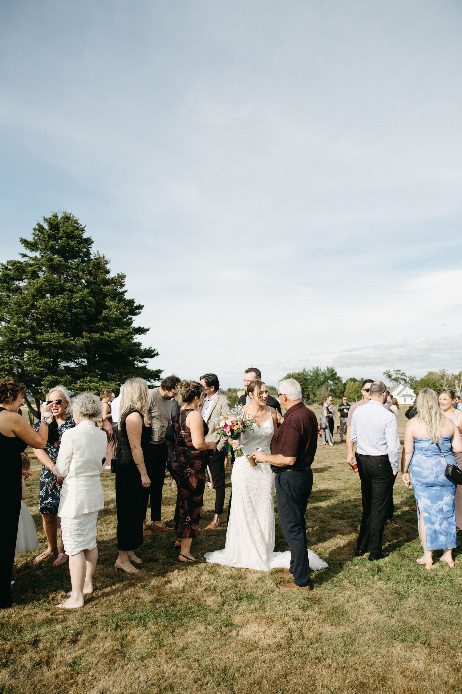 Wedding attendees gathered on a grassy hill under blue skies during an outdoor celebration.