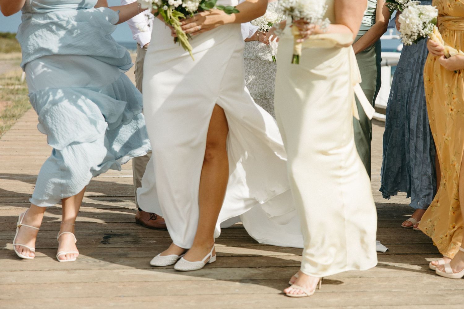 Detail shot of wedding party members' feet and dress hems on wooden dock.