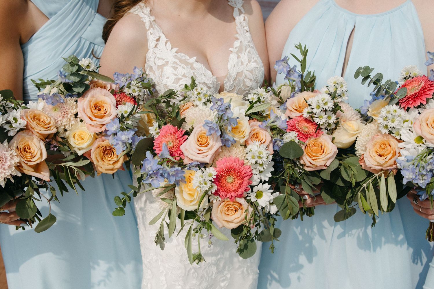 Elegant wedding bouquets featuring peach roses, coral flowers and blue accents against light blue dresses.